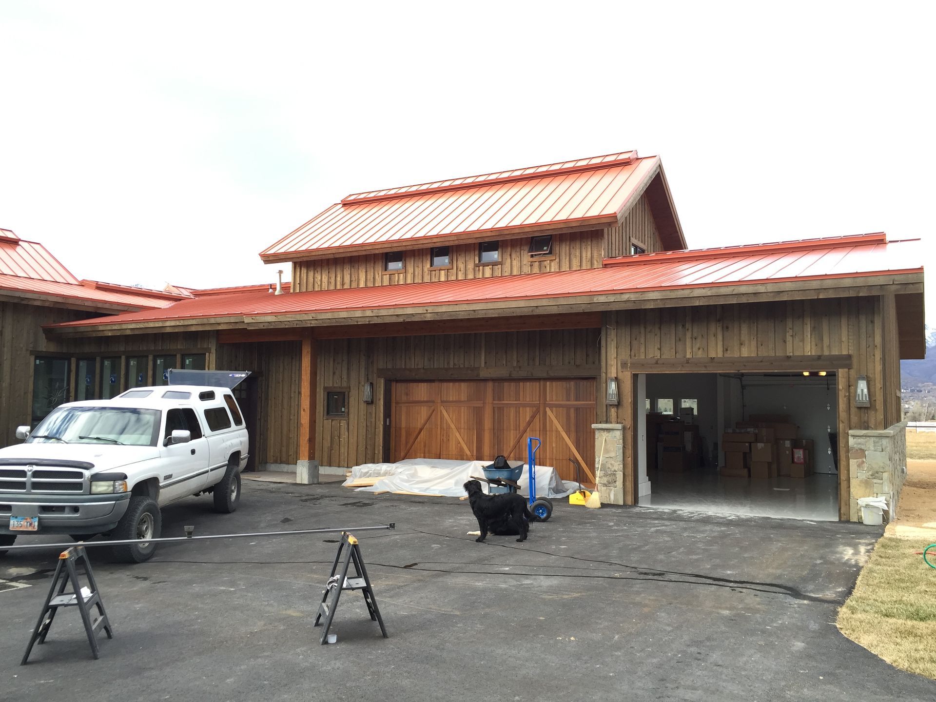 Rustic wooden barn with red metal roof, parked white truck, and driveway tools in front