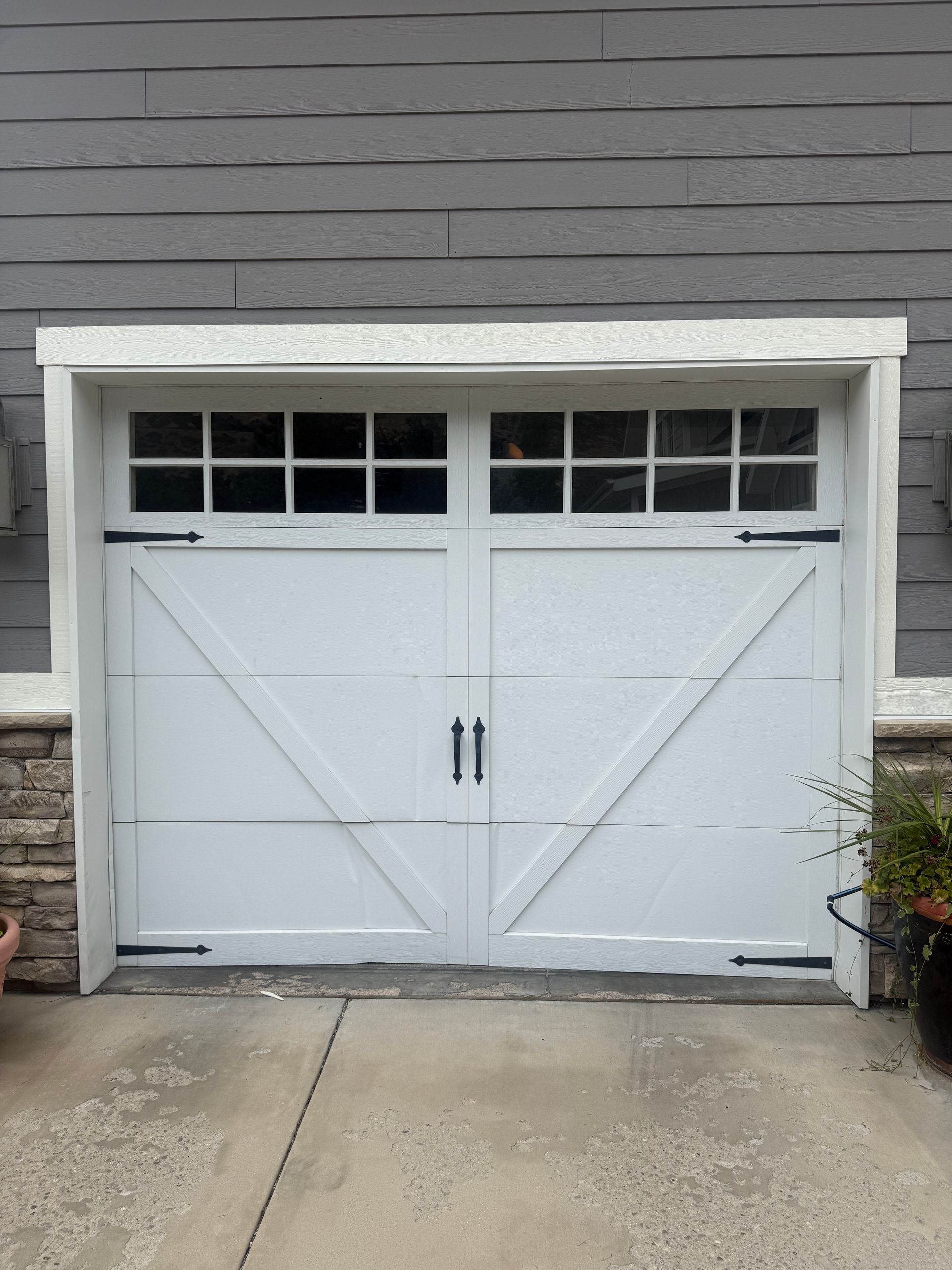 White double garage doors with small window panes on a gray house exterior