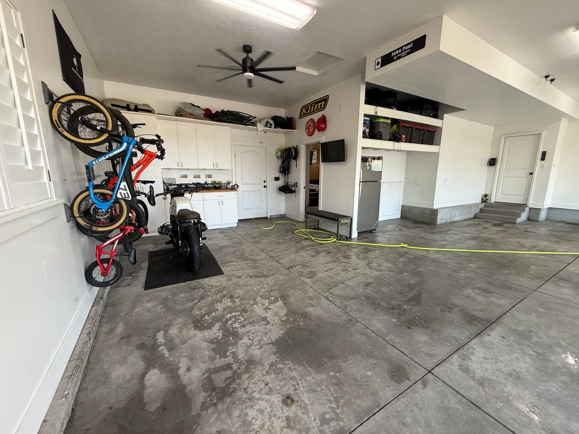 Garage interior with bikes on wall racks, a motorcycle, white cabinets, and a concrete floor