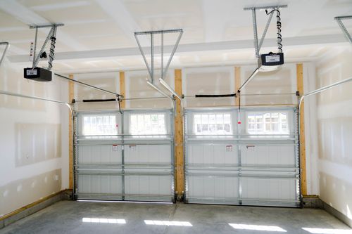 Empty two-car garage with white paneled doors and ceiling-mounted garage door openers.