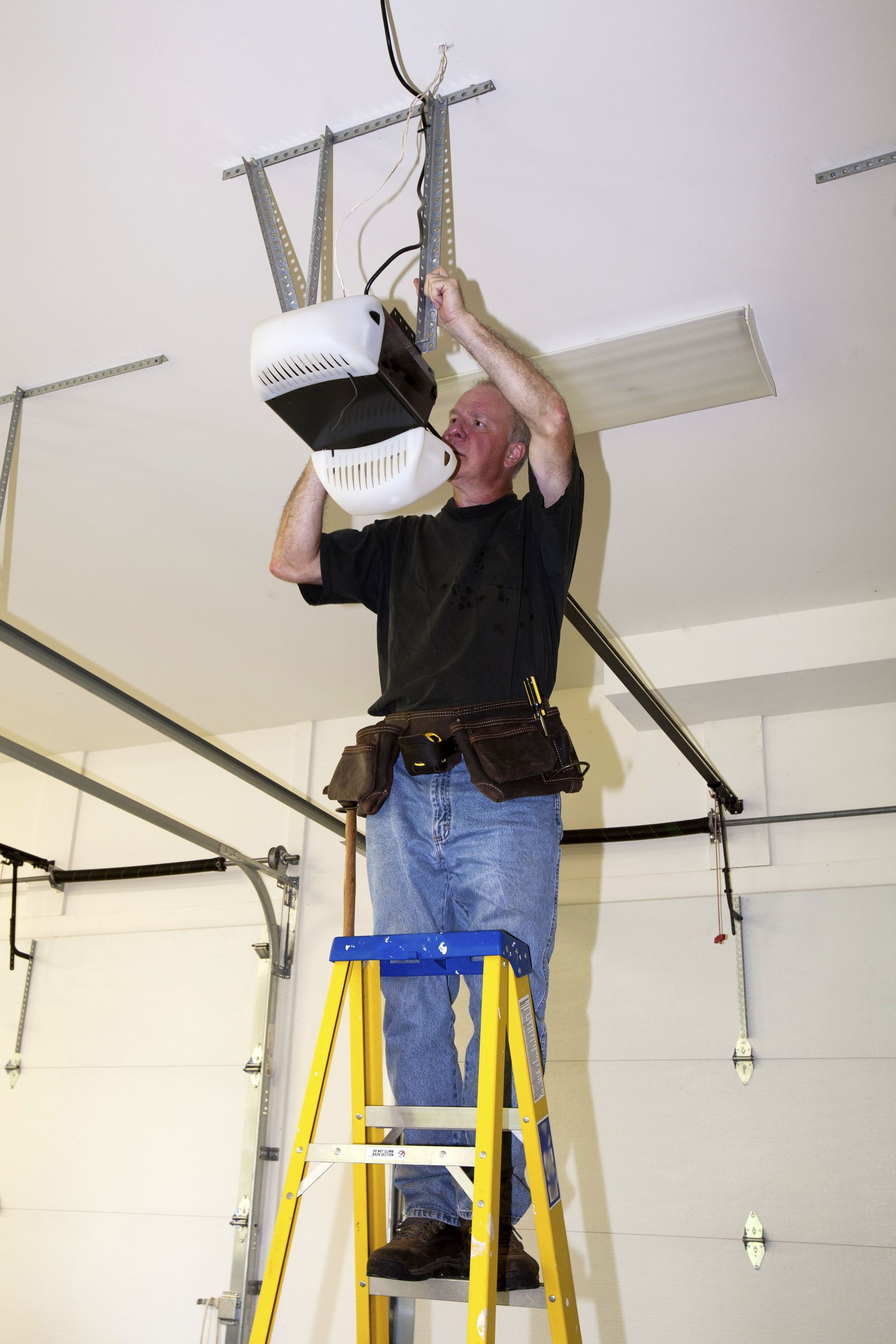 Person on a yellow ladder installing a garage door opener on a ceiling mount