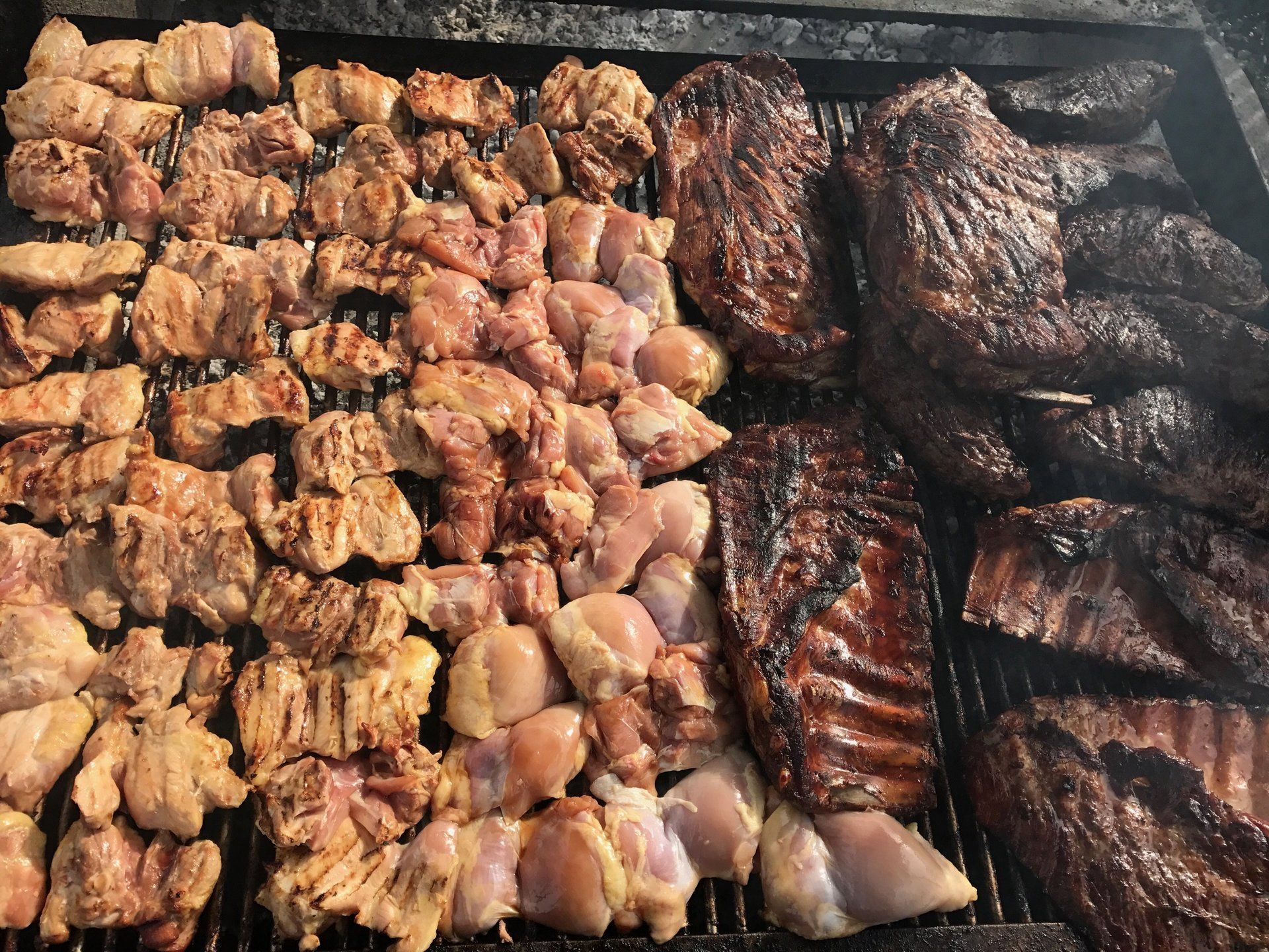Assorted grilled meats sizzling on a barbecue, including skewers and larger cuts.