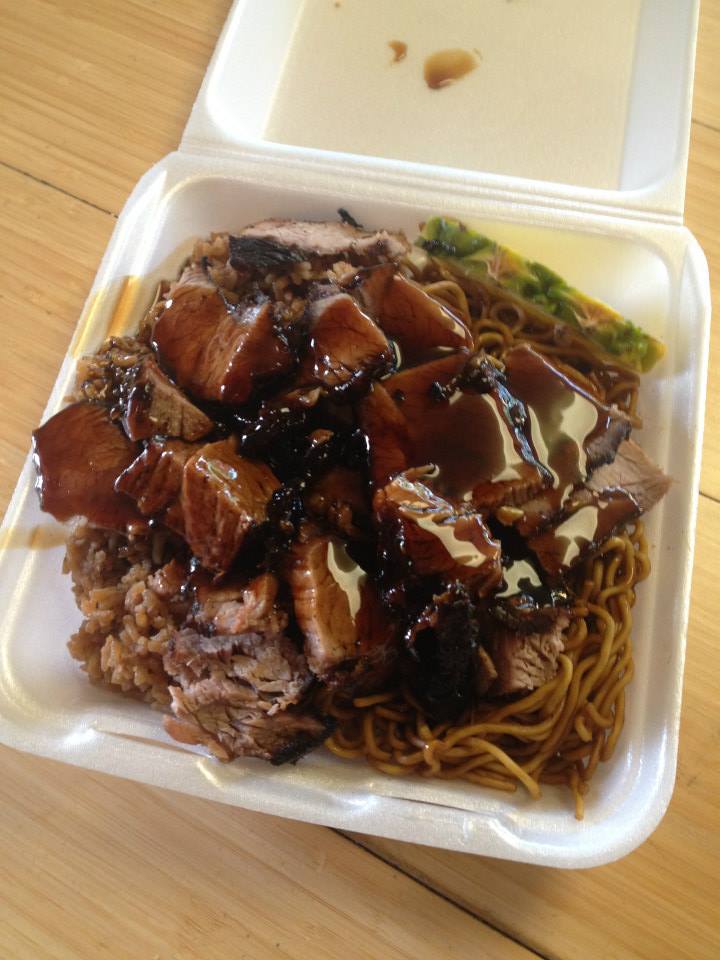 Takeout box with noodles topped with sliced roasted meat and dark sauce