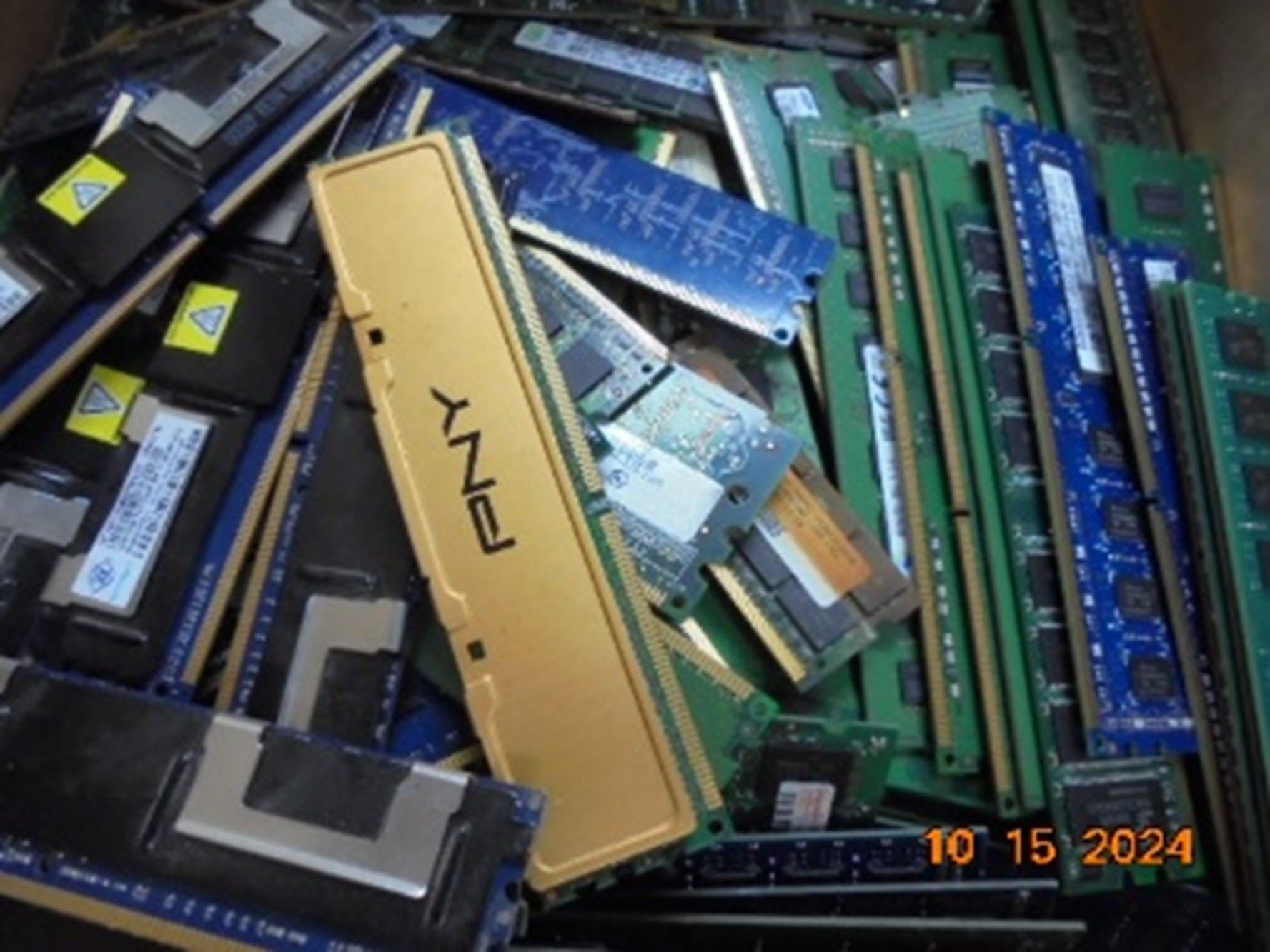 A cluttered pile of various computer RAM memory sticks in black, green, blue, and a prominent gold PNY module.