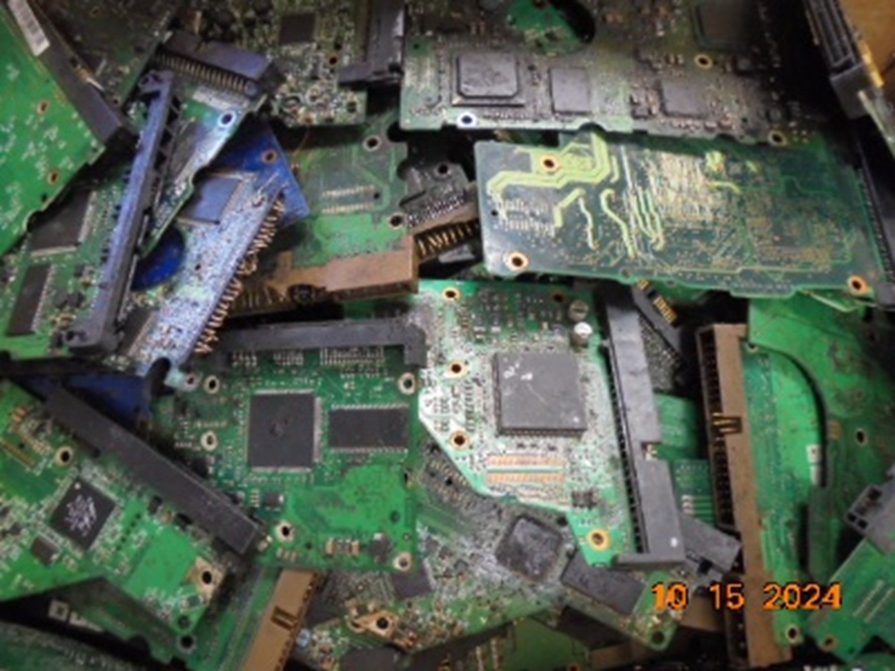 A large pile of disorganized, green electronic circuit boards from hard drives.