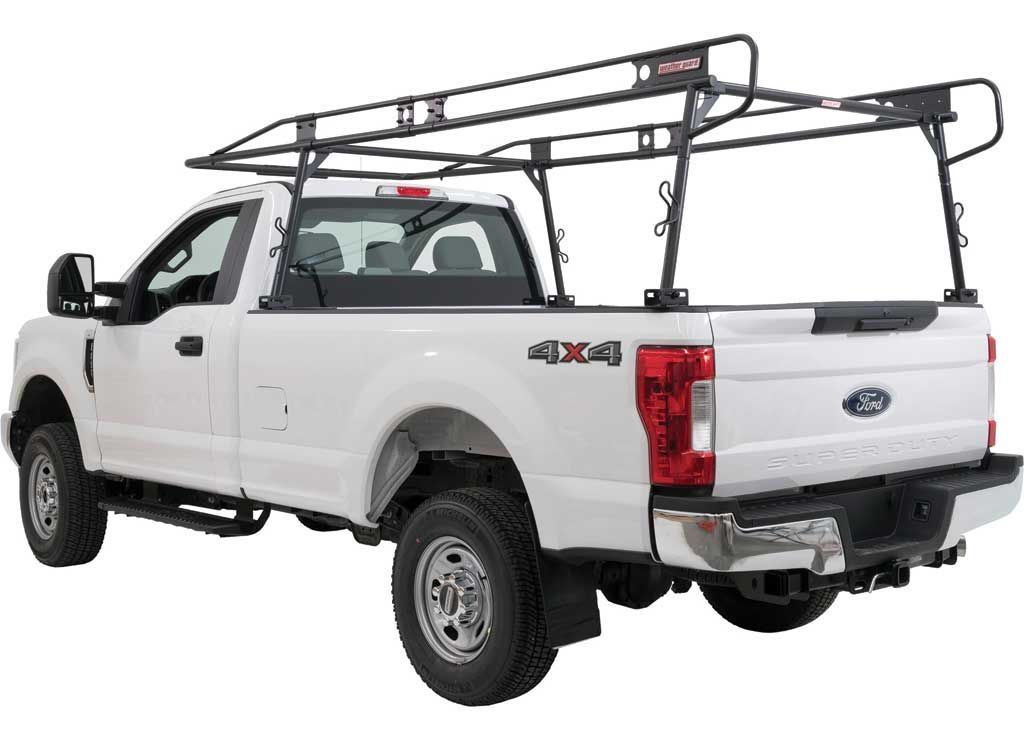 Black pickup truck with a raised dump bed parked by a river and mountains in the background