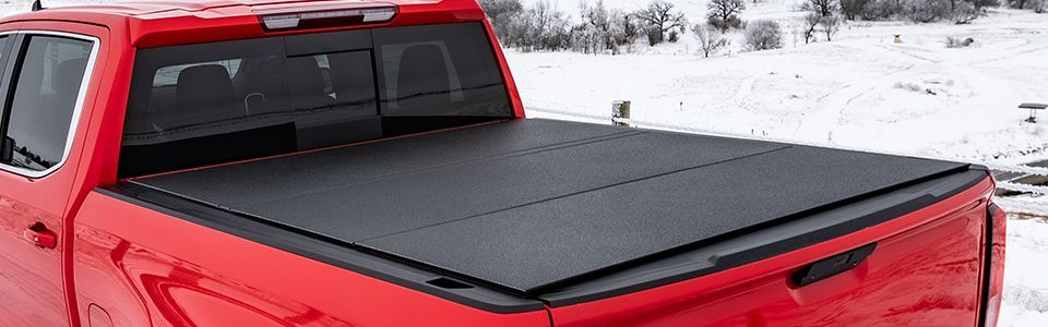 Dark gray pickup truck with a black tonneau cover parked near water on a snowy shoreline