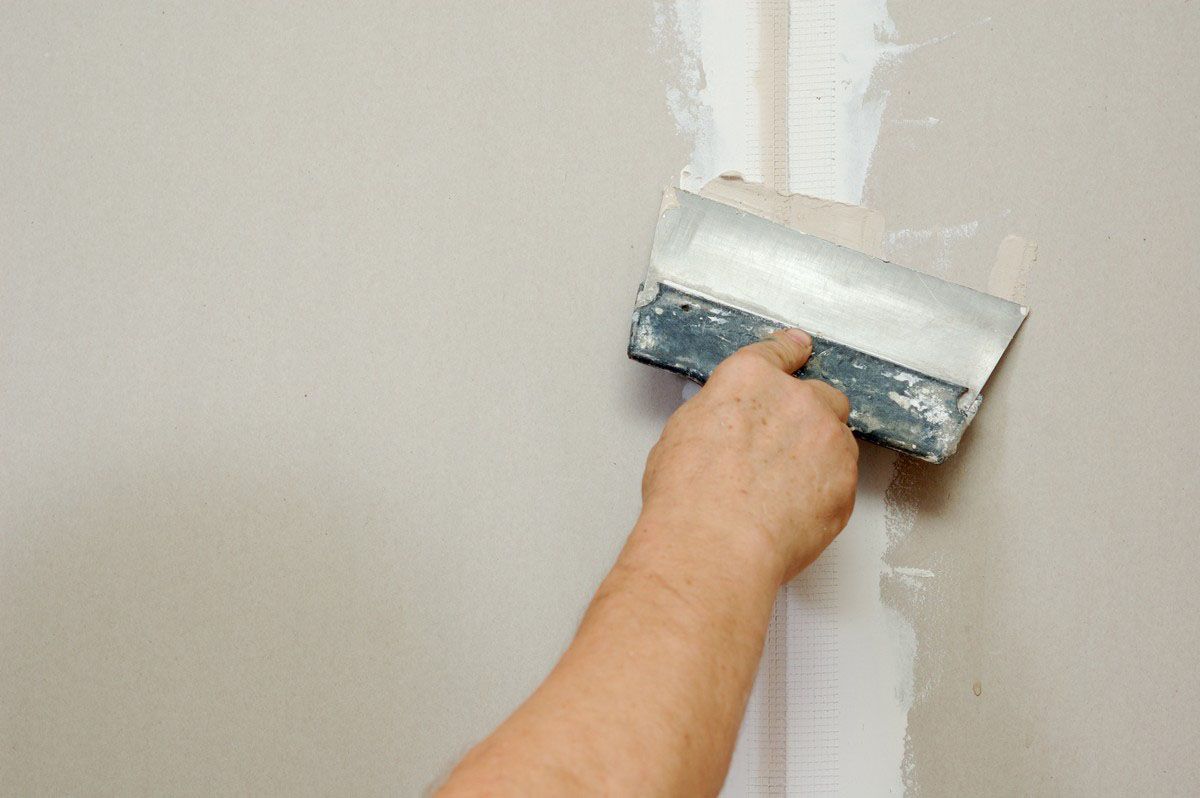 Person using a putty knife to apply joint compound on a wall.