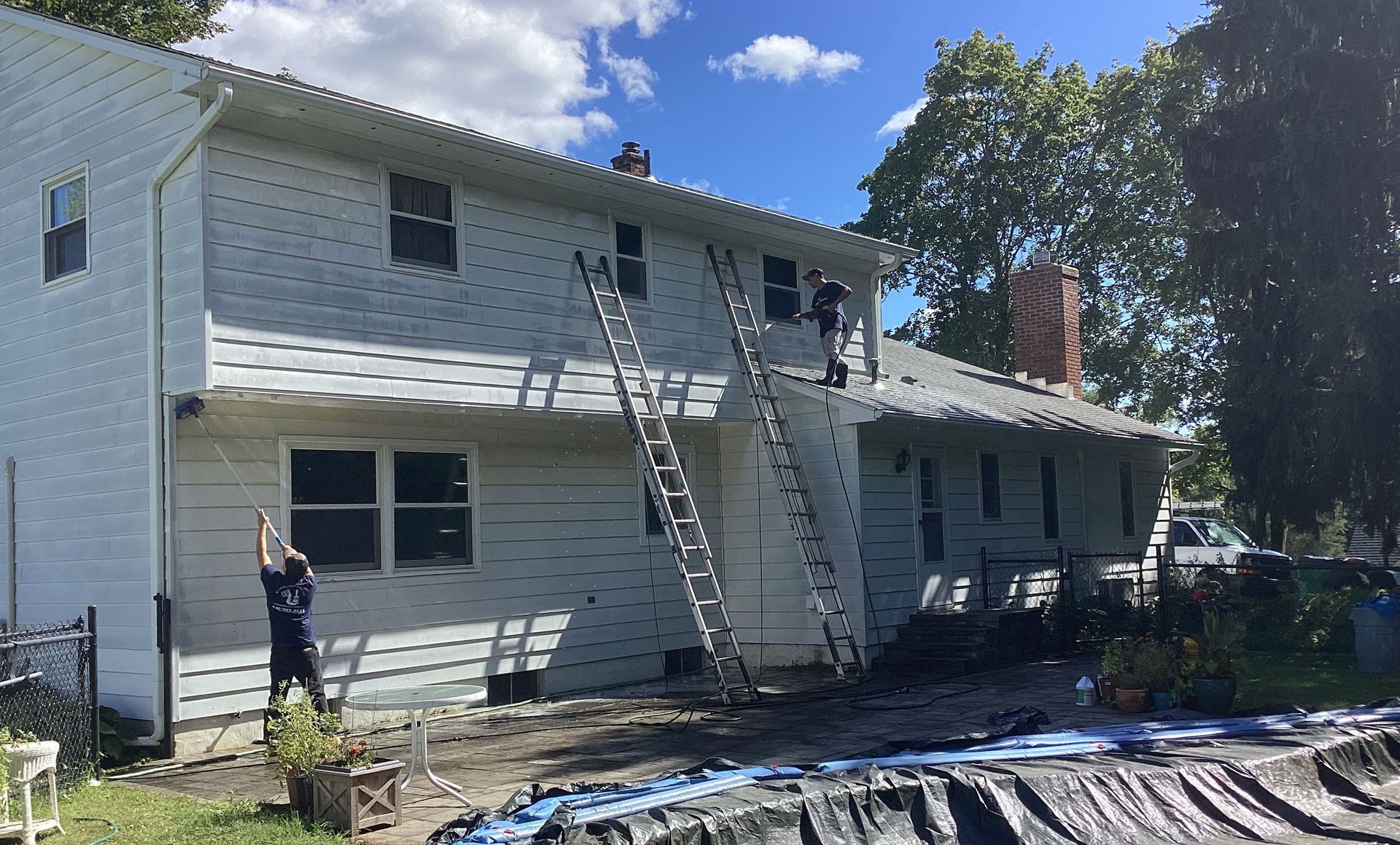 Workers install siding on a two-story house, using ladders.