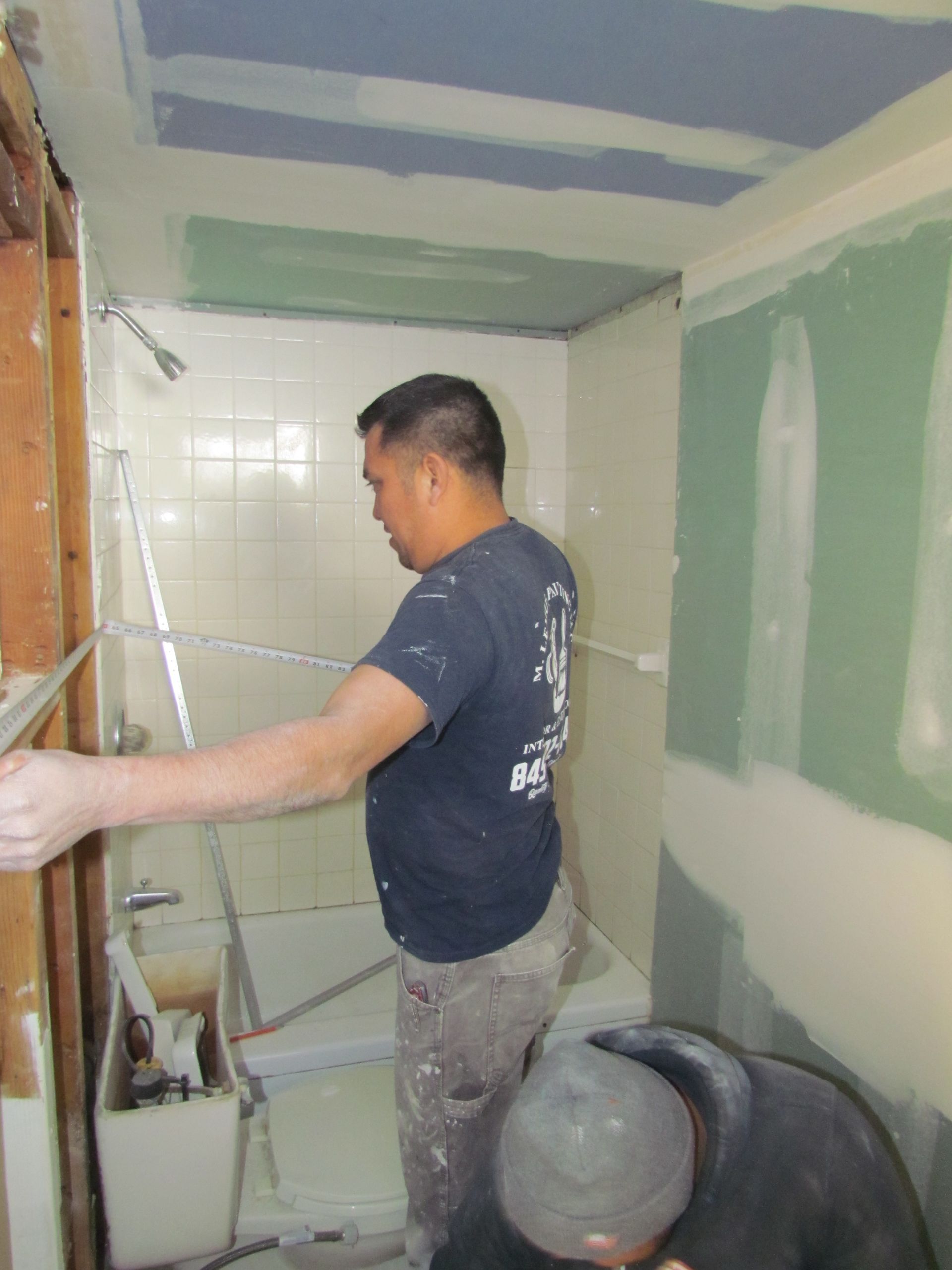 Man working on a bathroom renovation, installing drywall; interior shot.
