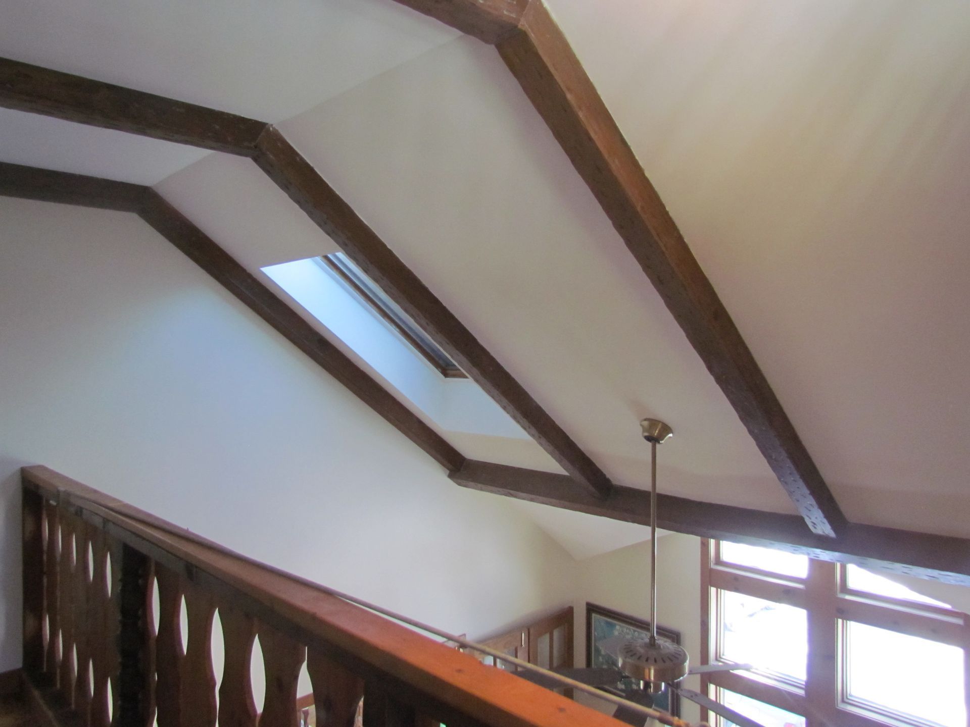 Wooden beams across a white ceiling with a skylight and a railing below.