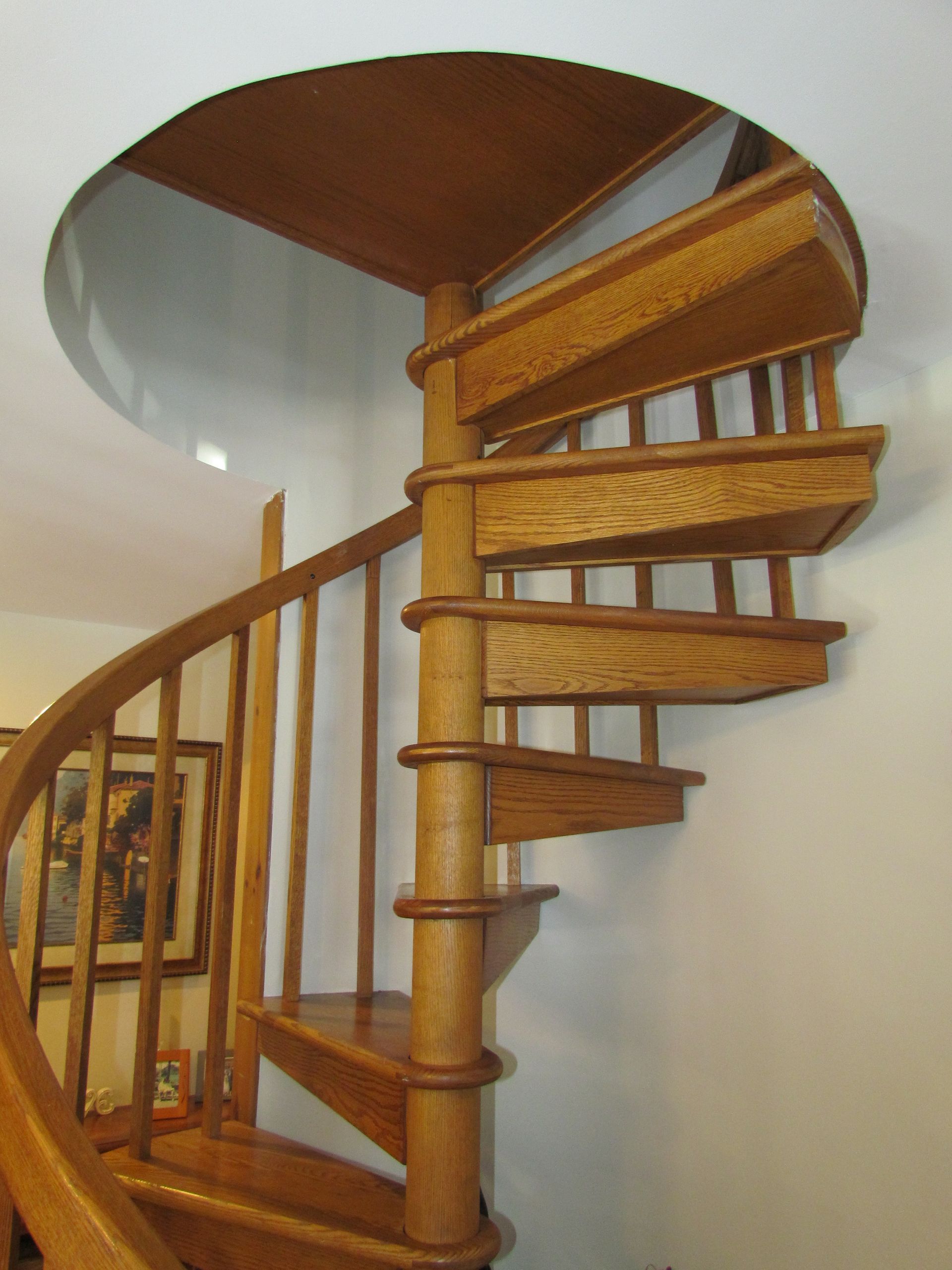 Wooden spiral staircase ascending to a circular opening in the ceiling; beige walls.