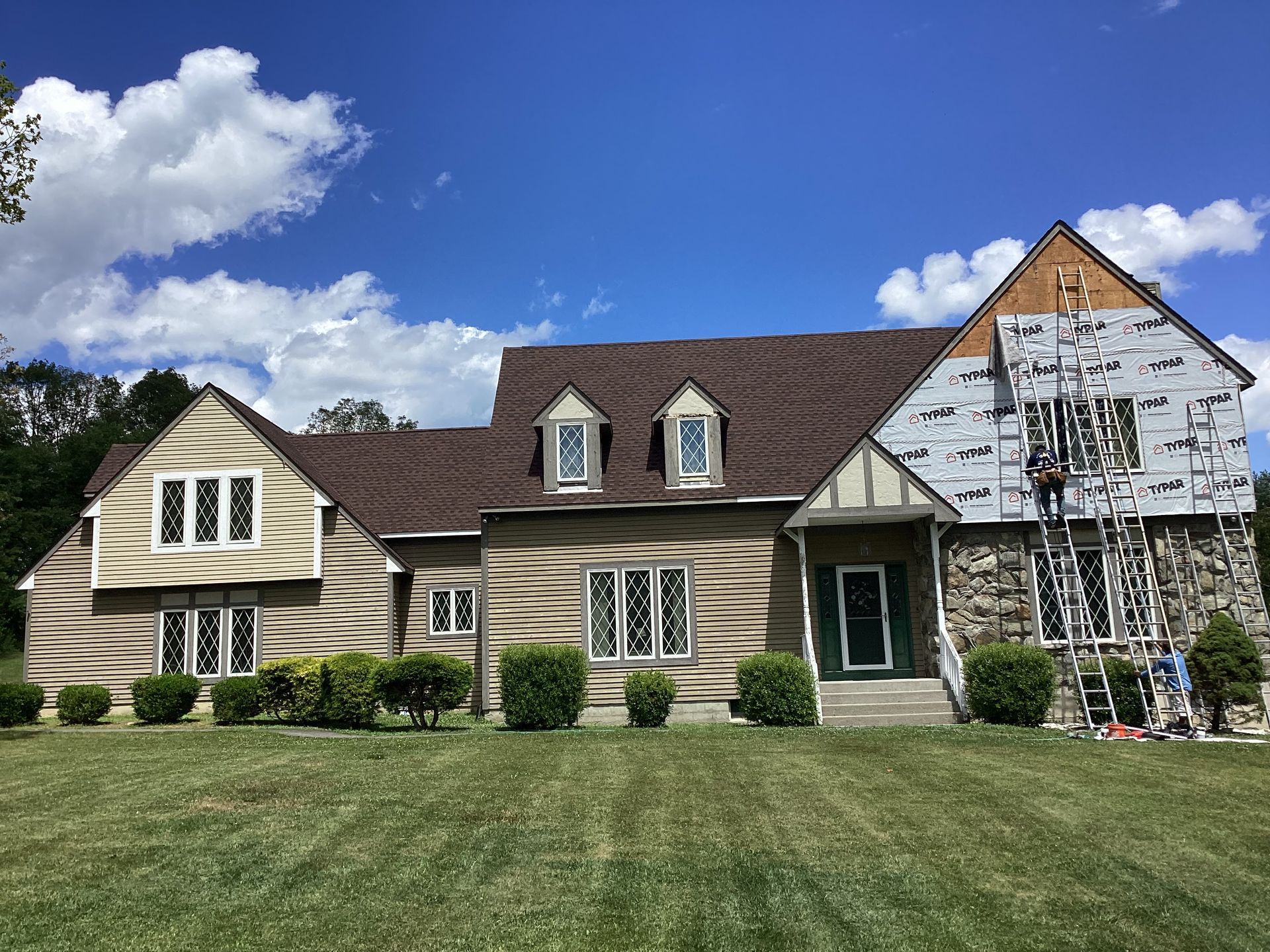 House with new brown roof and siding being installed. Blue sky and grass.