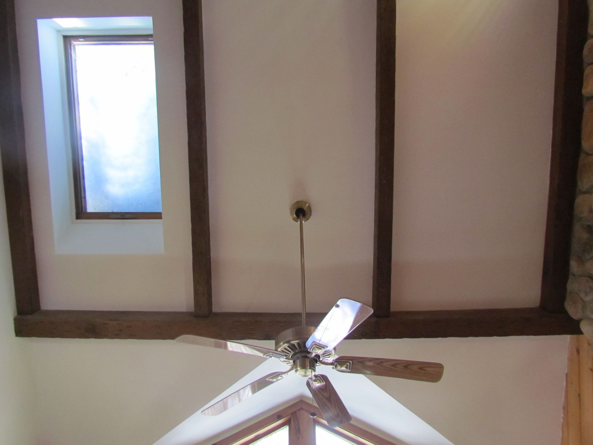 Ceiling with beams, skylight, and ceiling fan. White walls, wood accents, natural light.