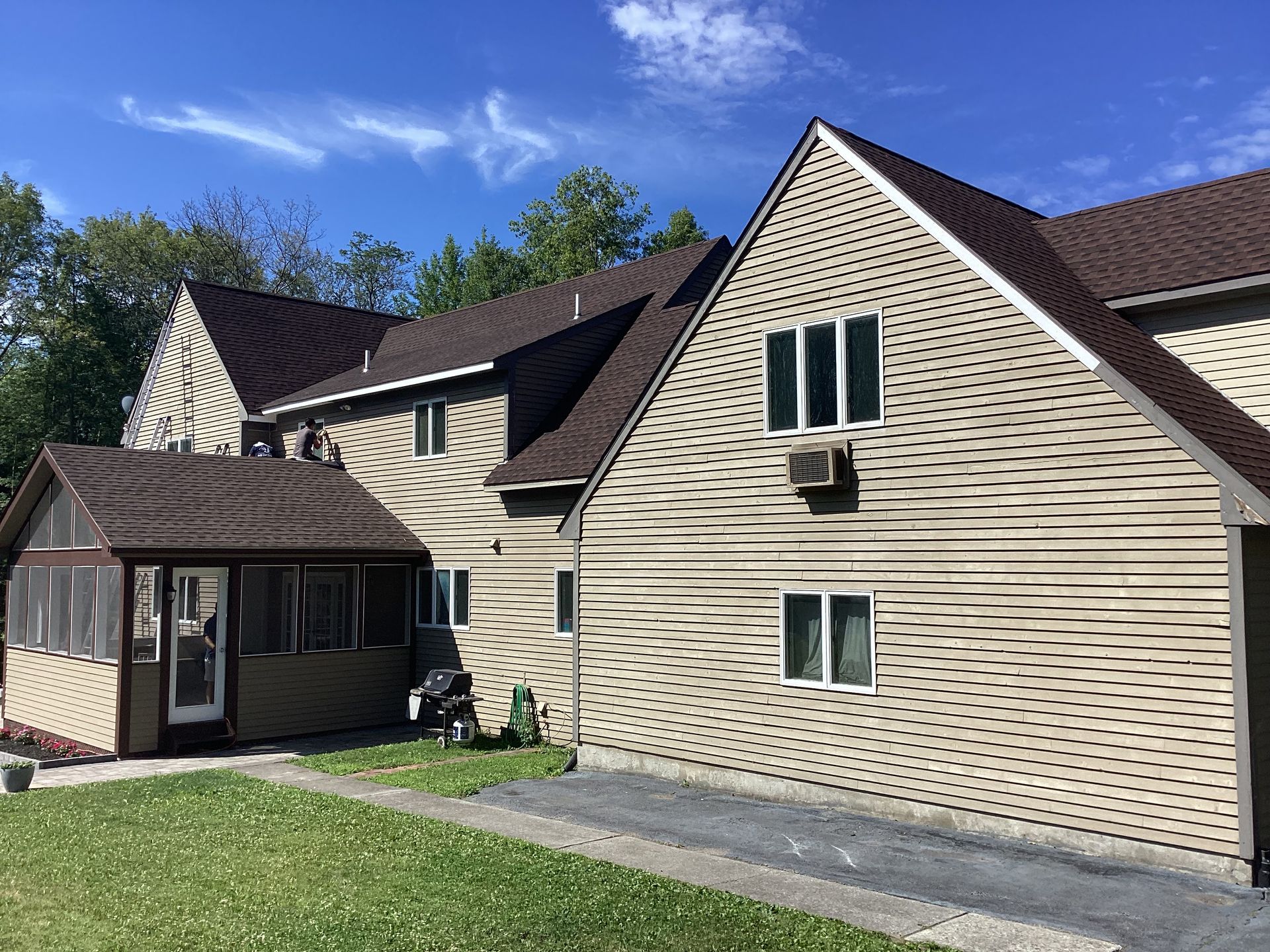 Tan multi-unit building with brown roof and siding, green grass, and blue sky.