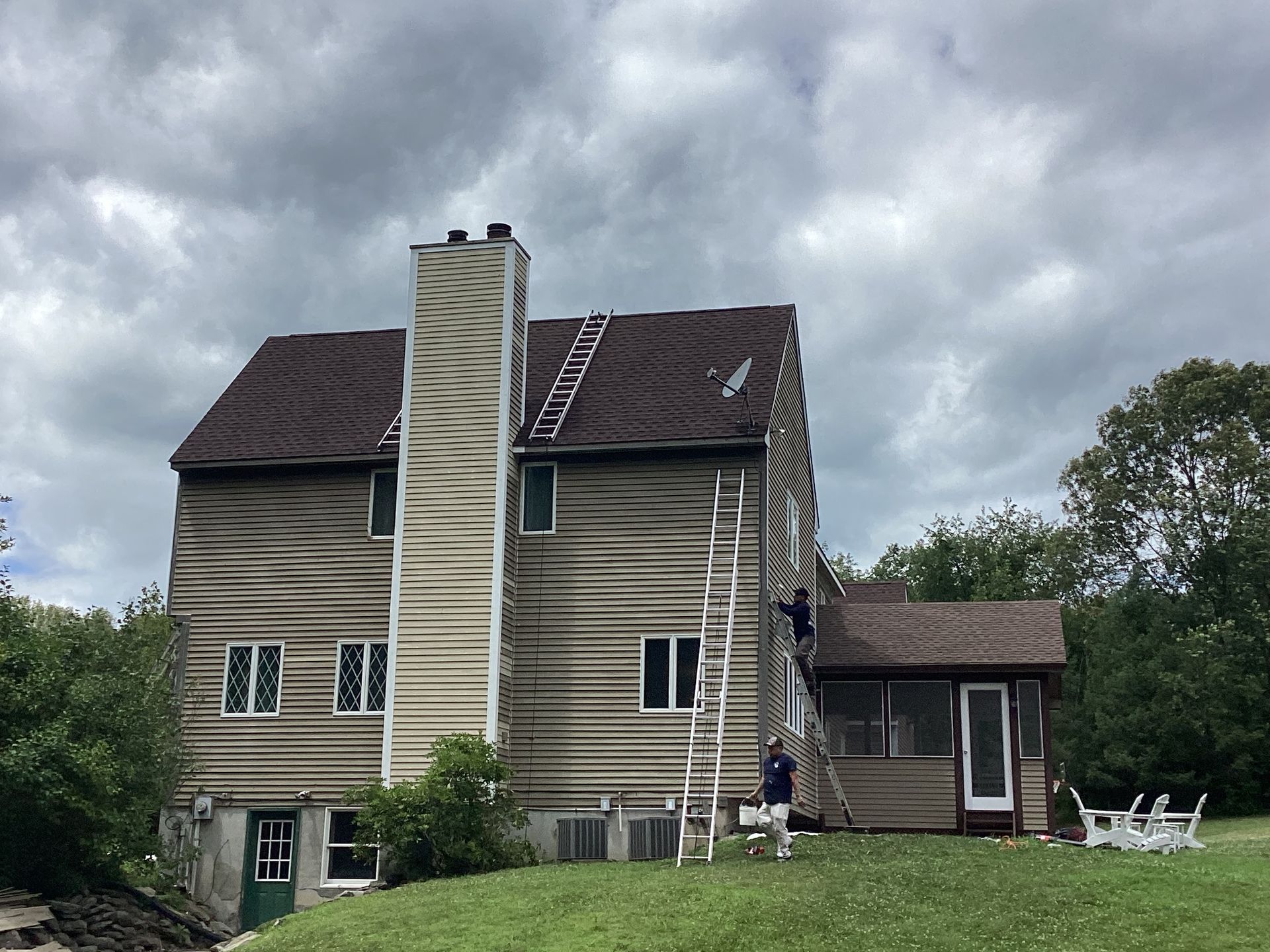 Two-story house with workers on ladders near the roof. Overcast day.