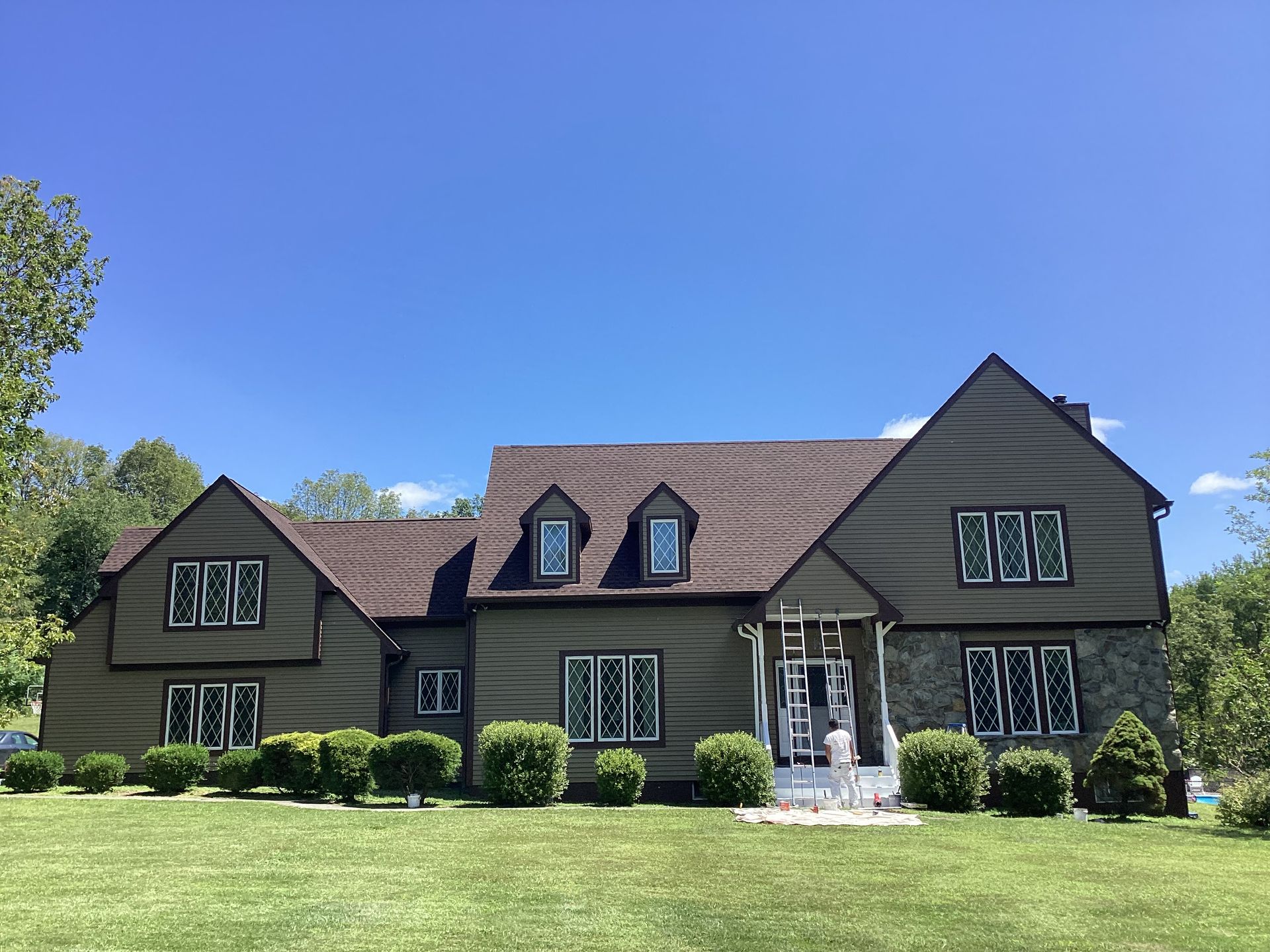 Two-story house with green siding, brown roof, and stone facade under a clear blue sky.