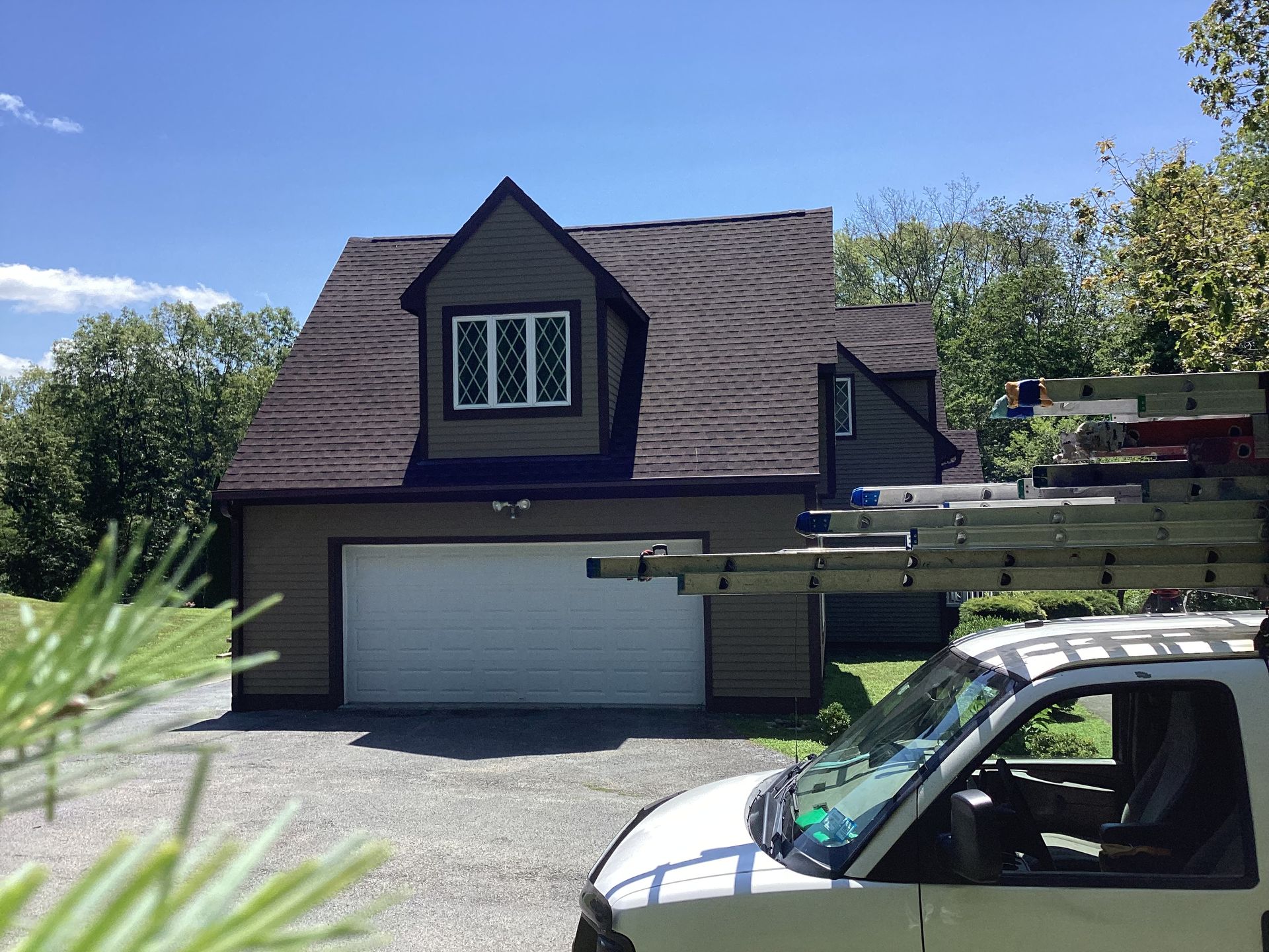 Garage with brown roof, tan siding, and a white garage door, with a white truck parked in front.