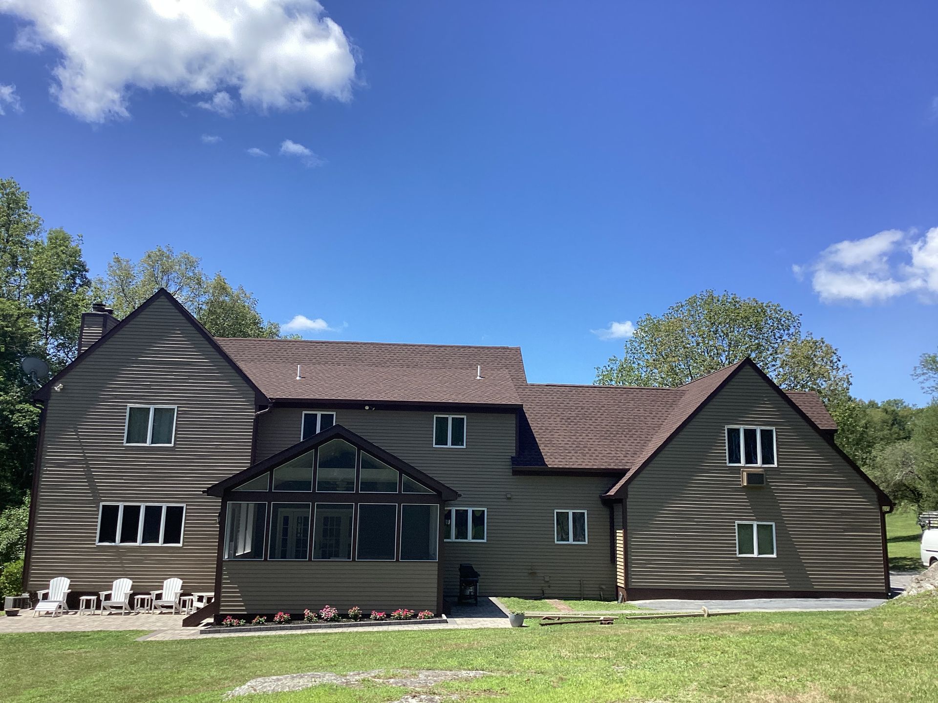 Two-story brown house with white windows and a screened-in porch under a blue sky.