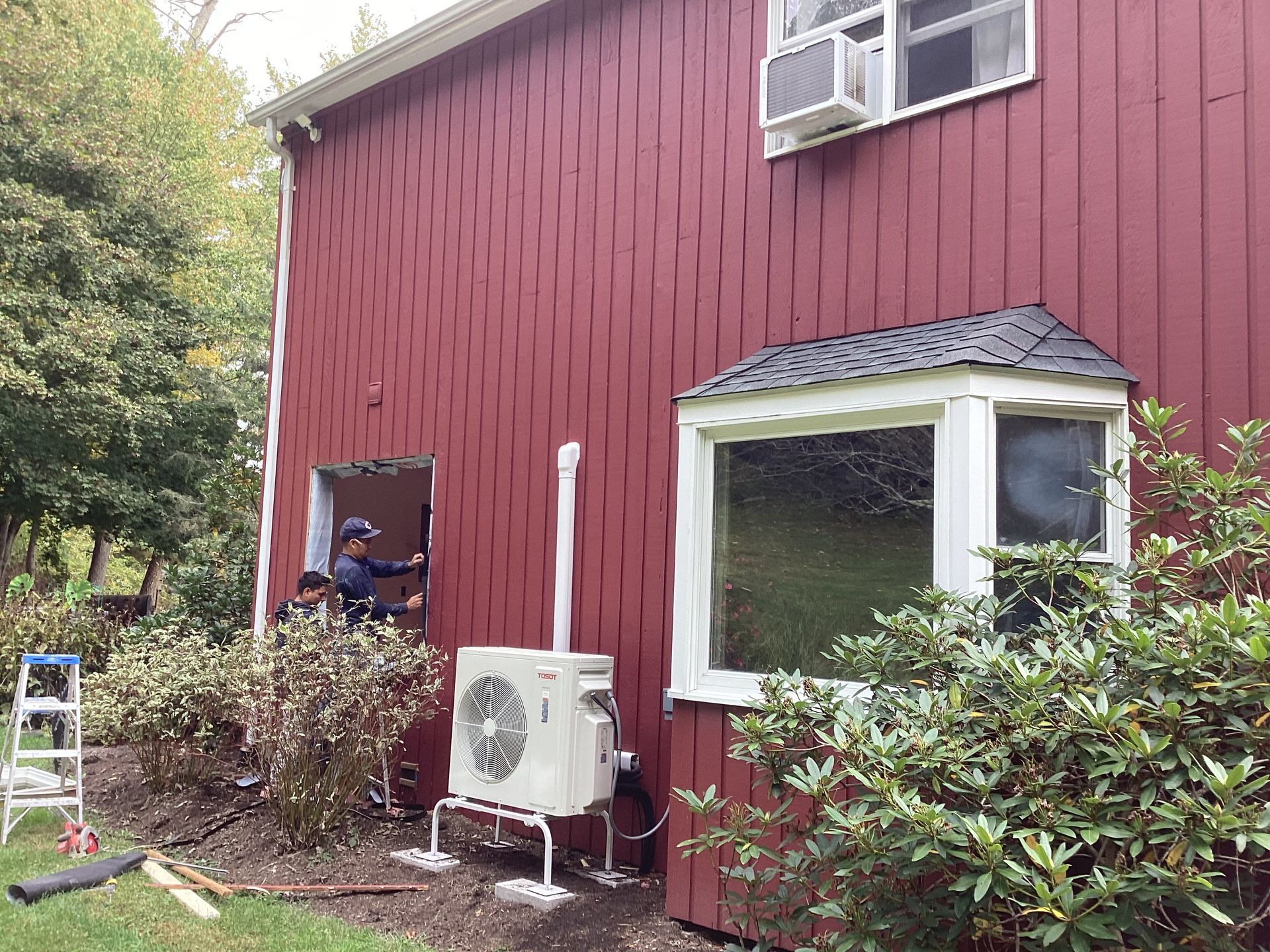 Red house with an AC unit being installed; a person works from an open doorway.