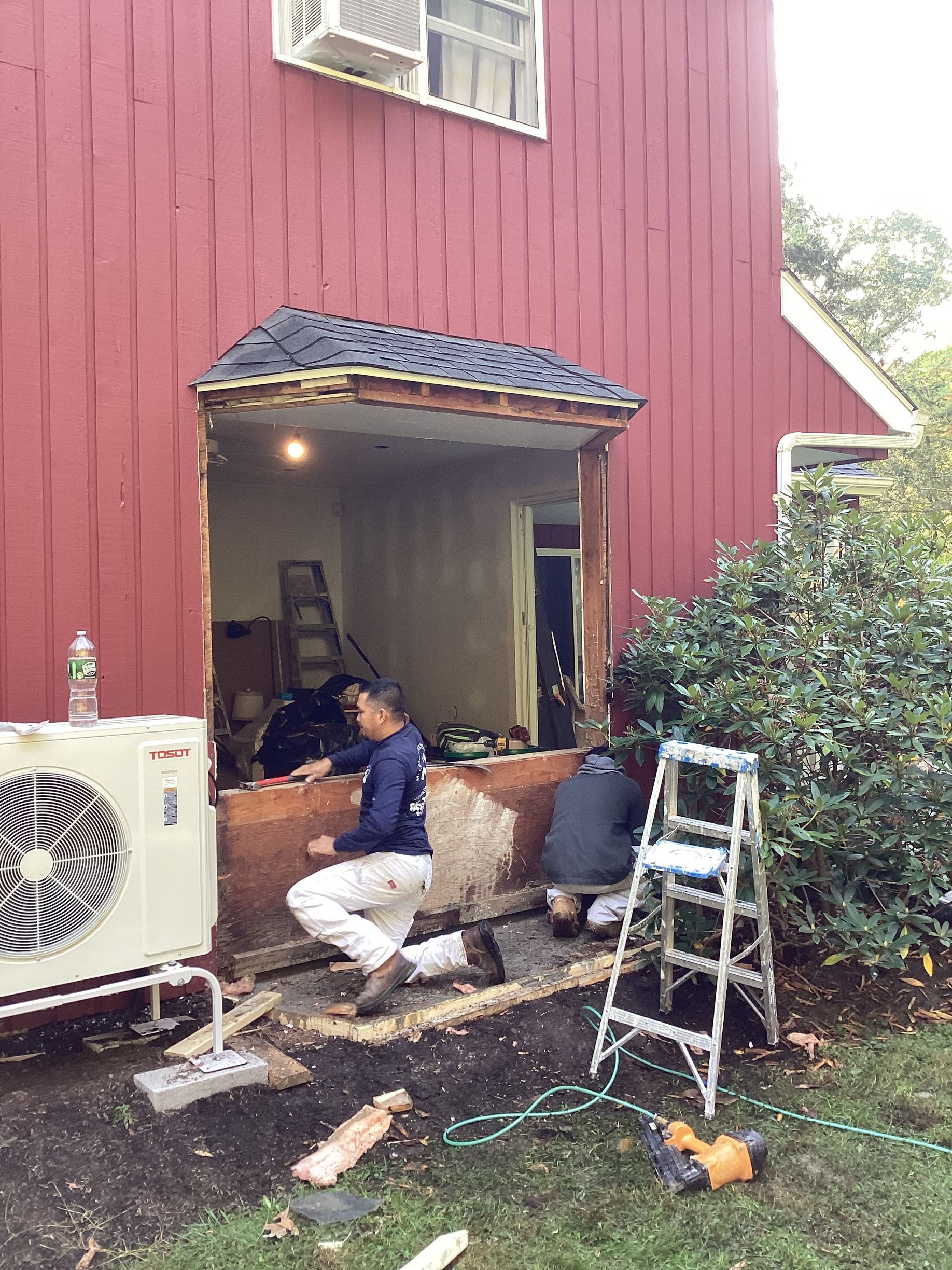 Construction workers removing siding from a red house; a window opening.