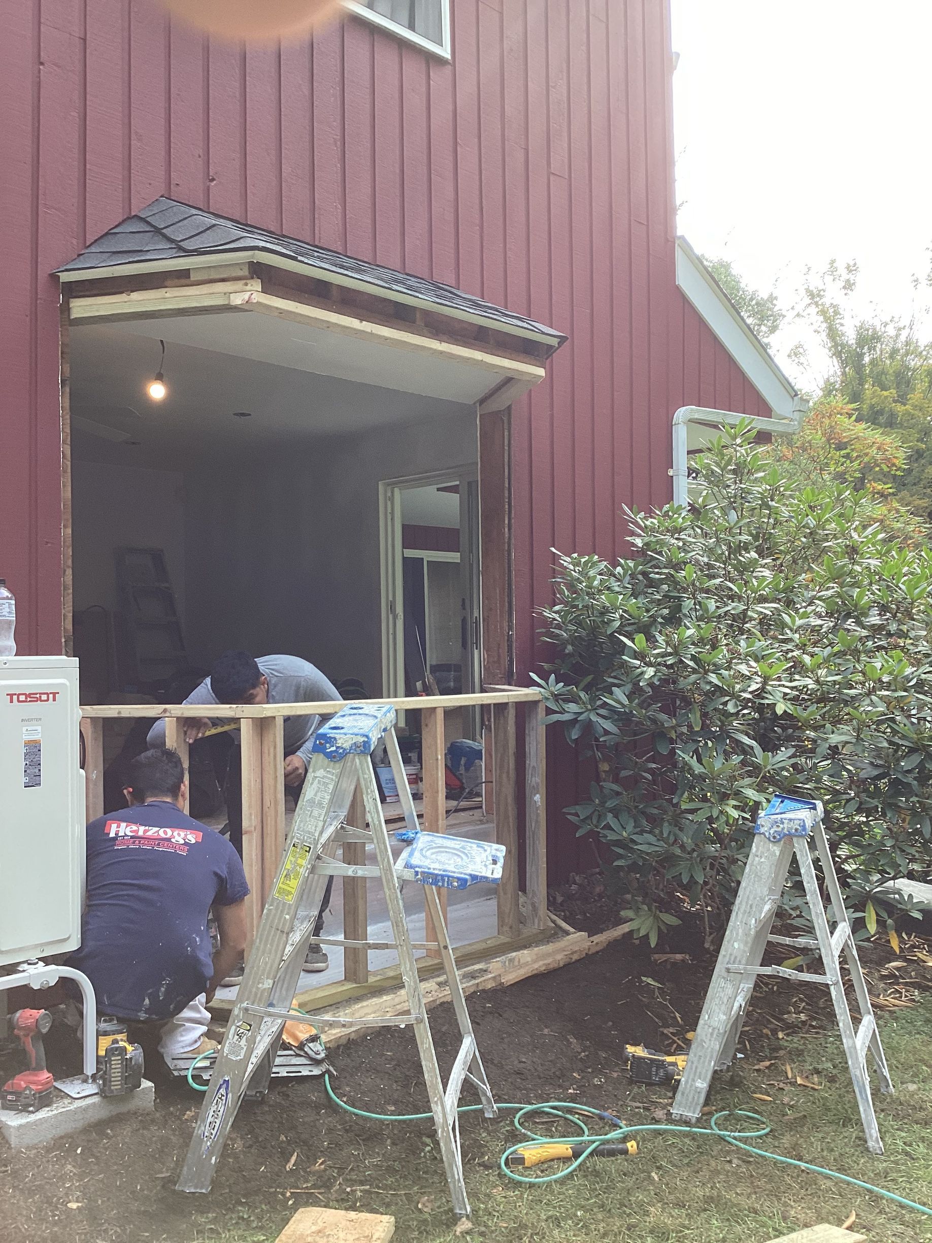 Workers building a porch on a red building.  Two ladders and tools are present.