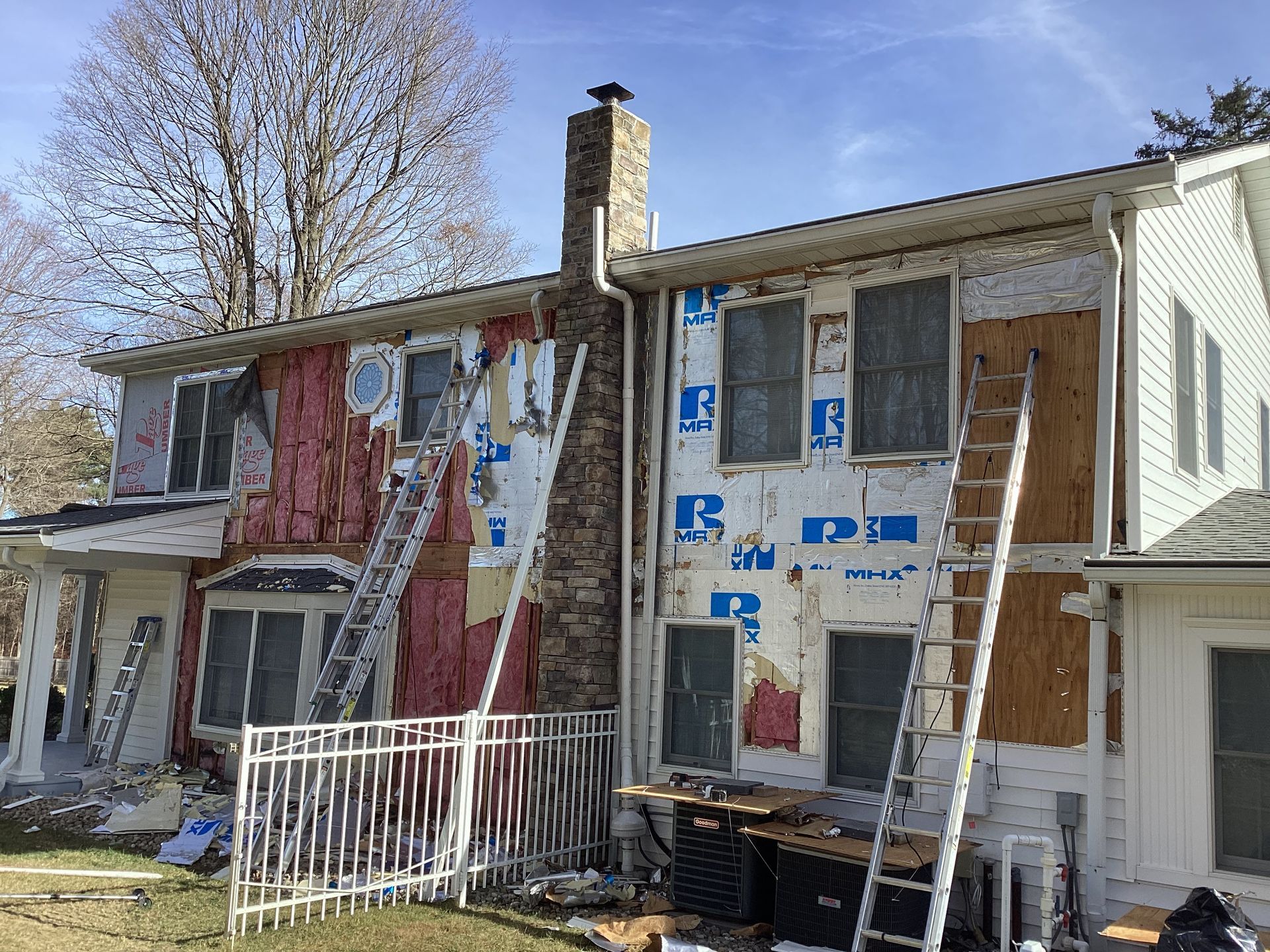 House undergoing siding replacement; exposed walls with insulation and ladders, in daylight.