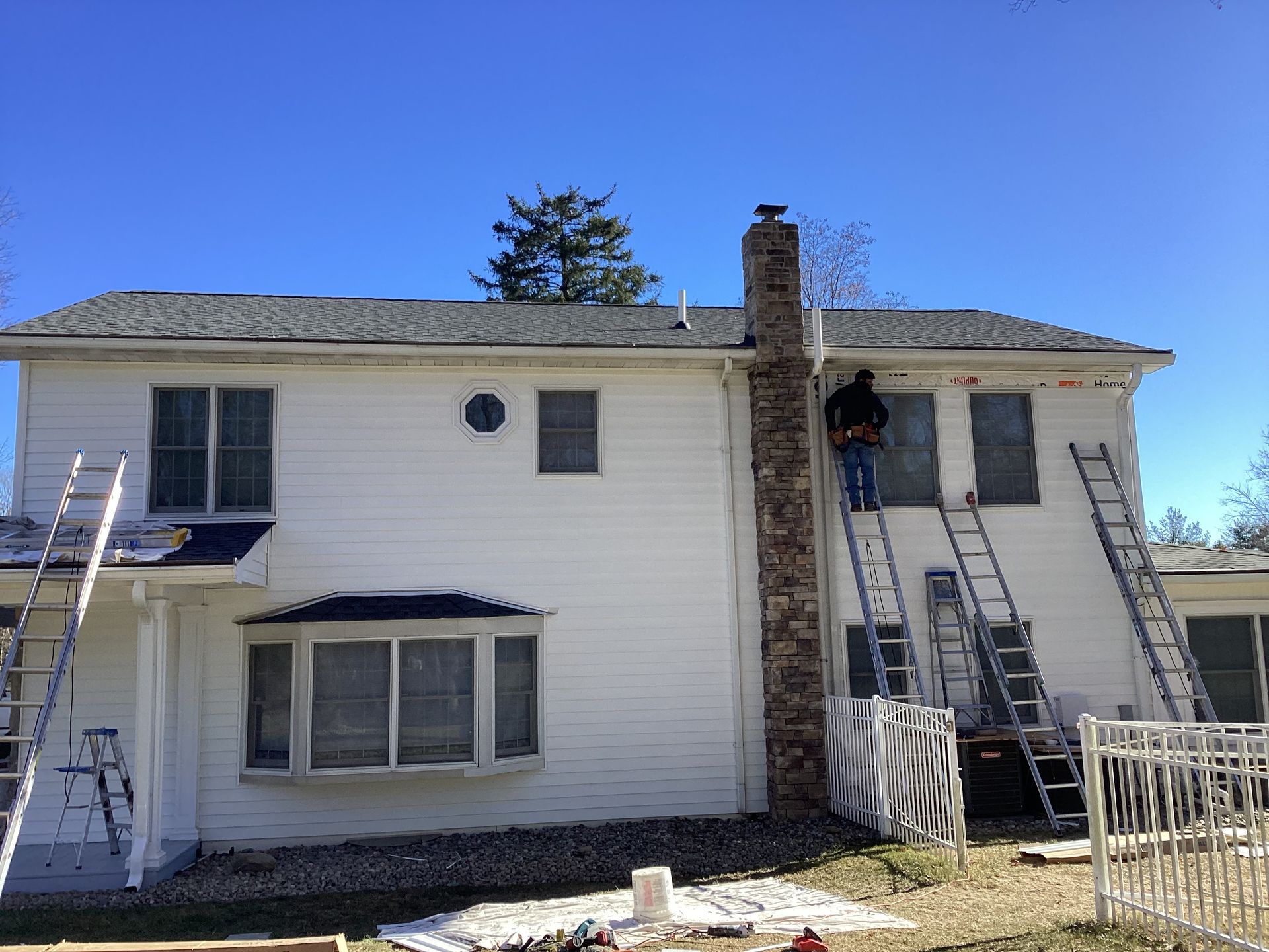 Two-story white house; person on chimney, ladders against walls, sunny day.