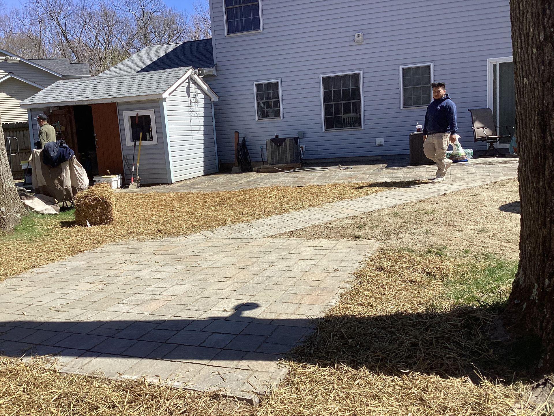 Backyard with a person walking on a stone path, shed, and house.