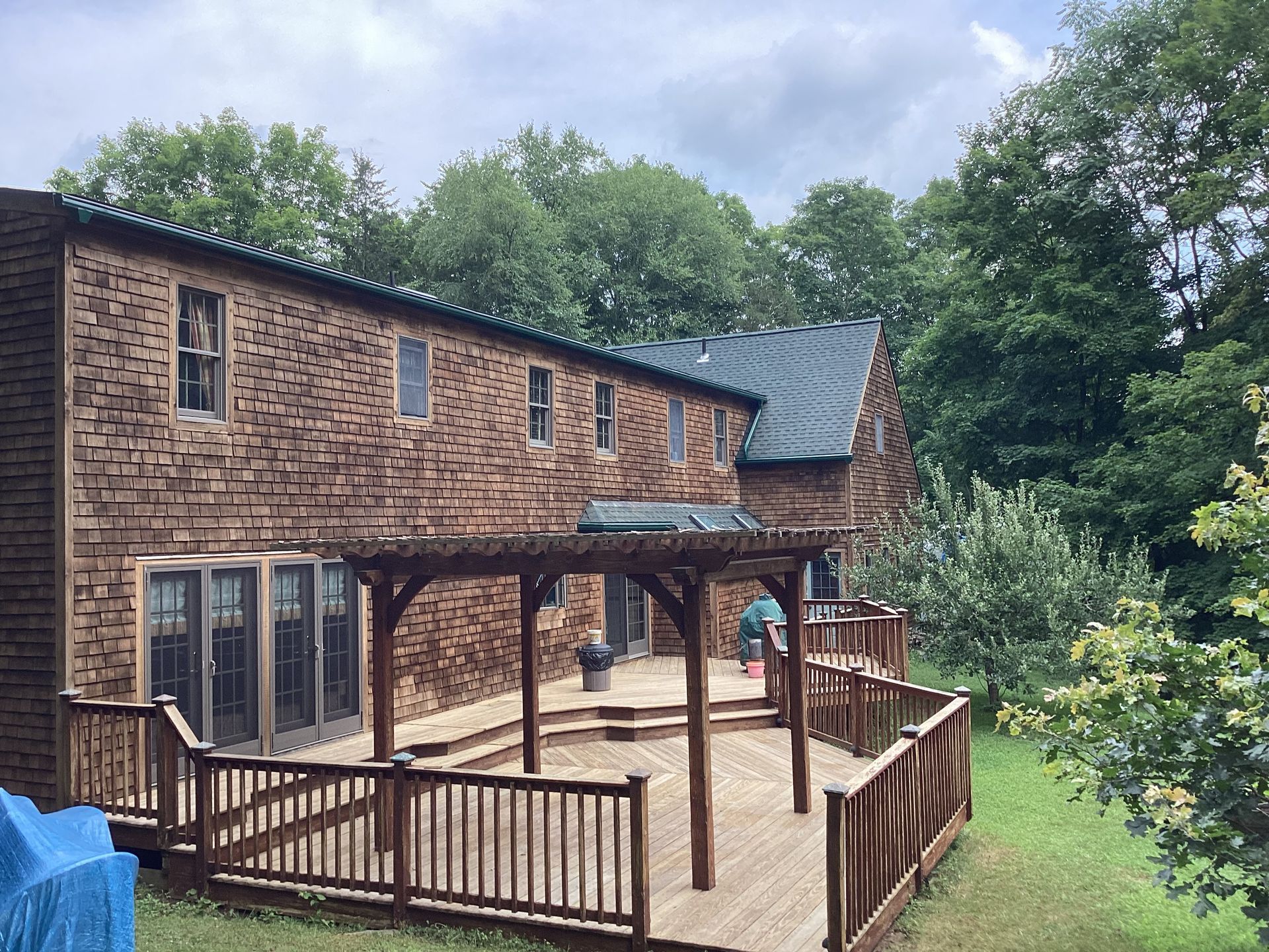 Brick house with wooden deck and pergola, surrounded by trees.