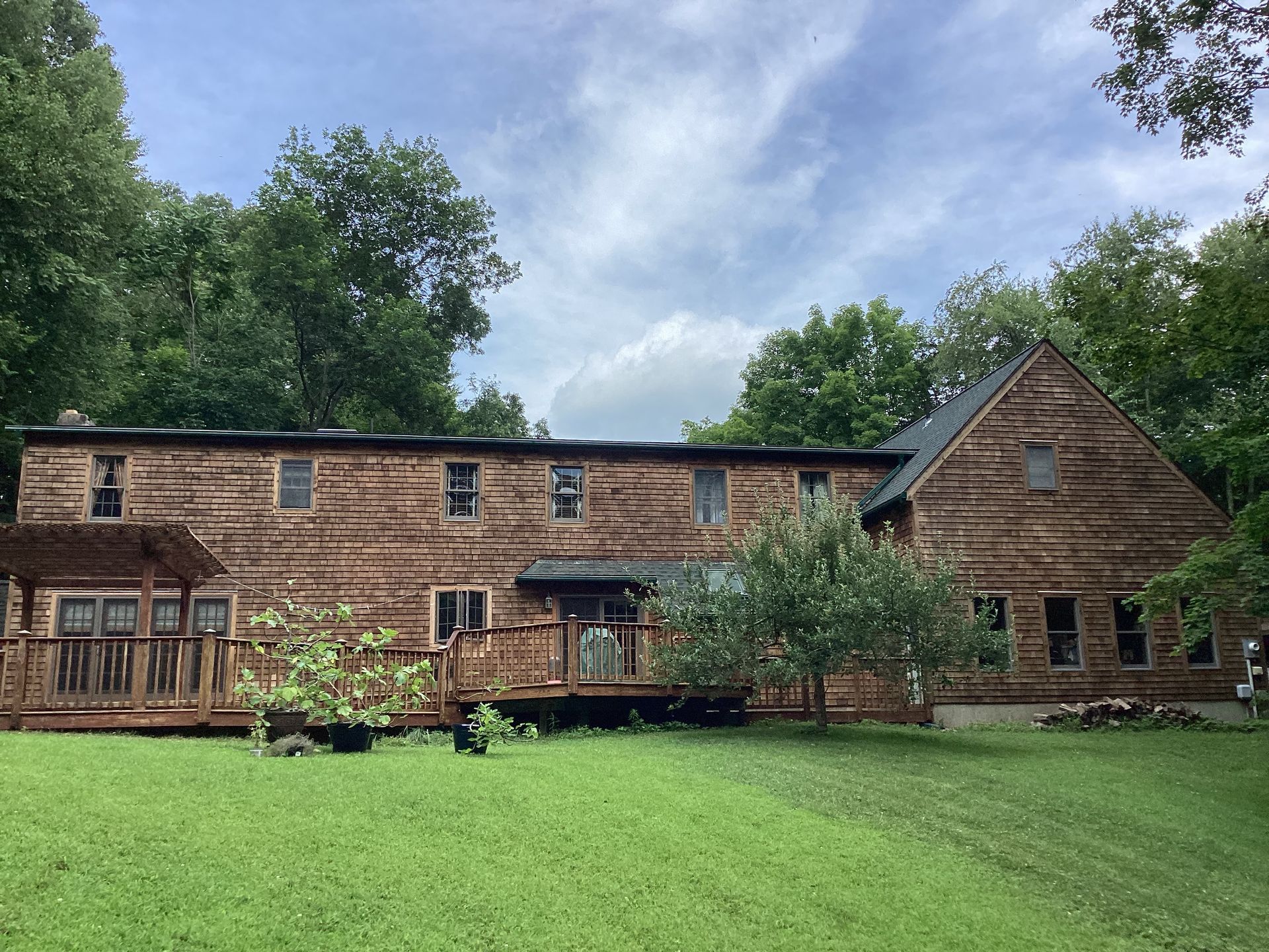Log cabin style house with green lawn, trees, and cloudy sky.