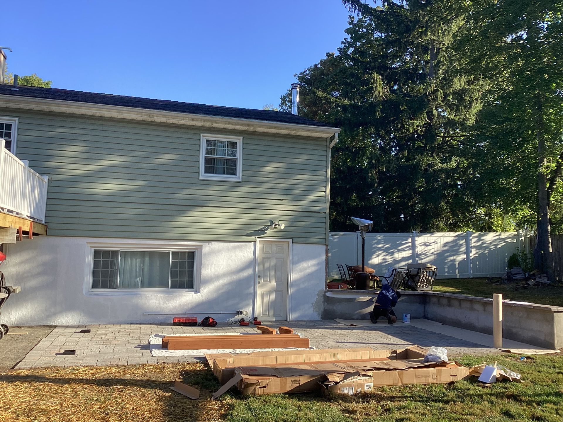Back of a house with a concrete patio and construction materials, blue sky and green tree.