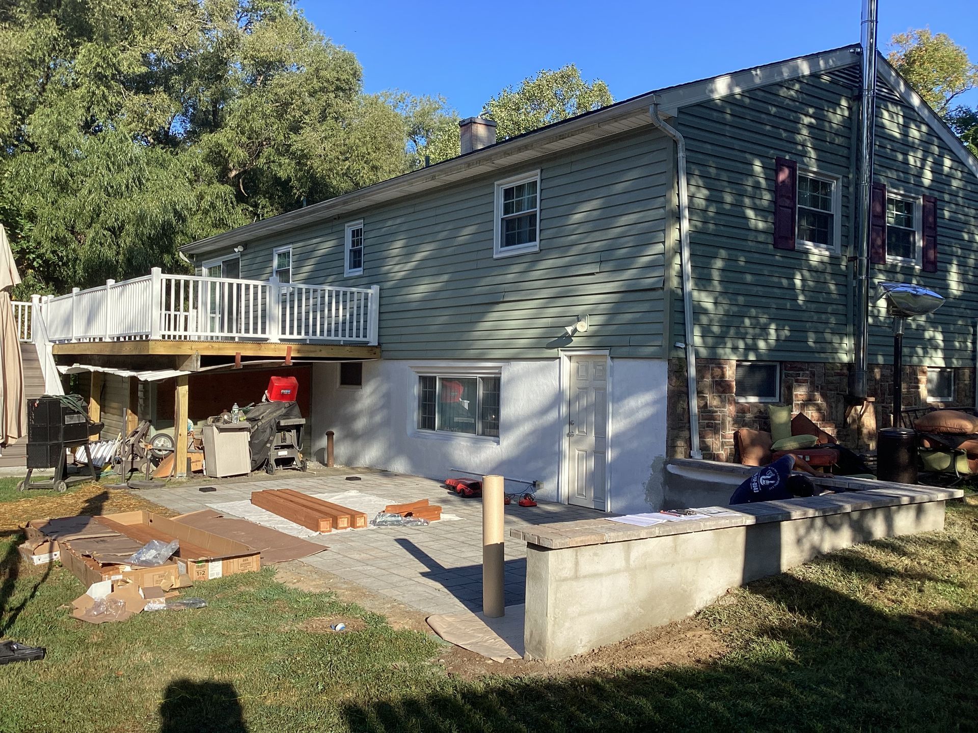 Back of a house with a deck under construction; green siding, white railings, and a gray patio.