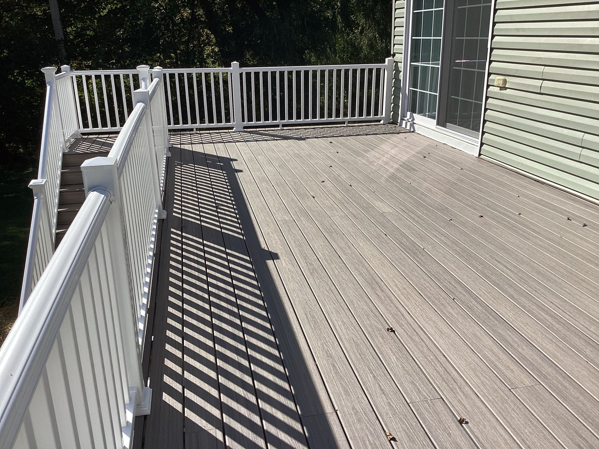 Deck with white railing and composite flooring, with shadows cast across it.