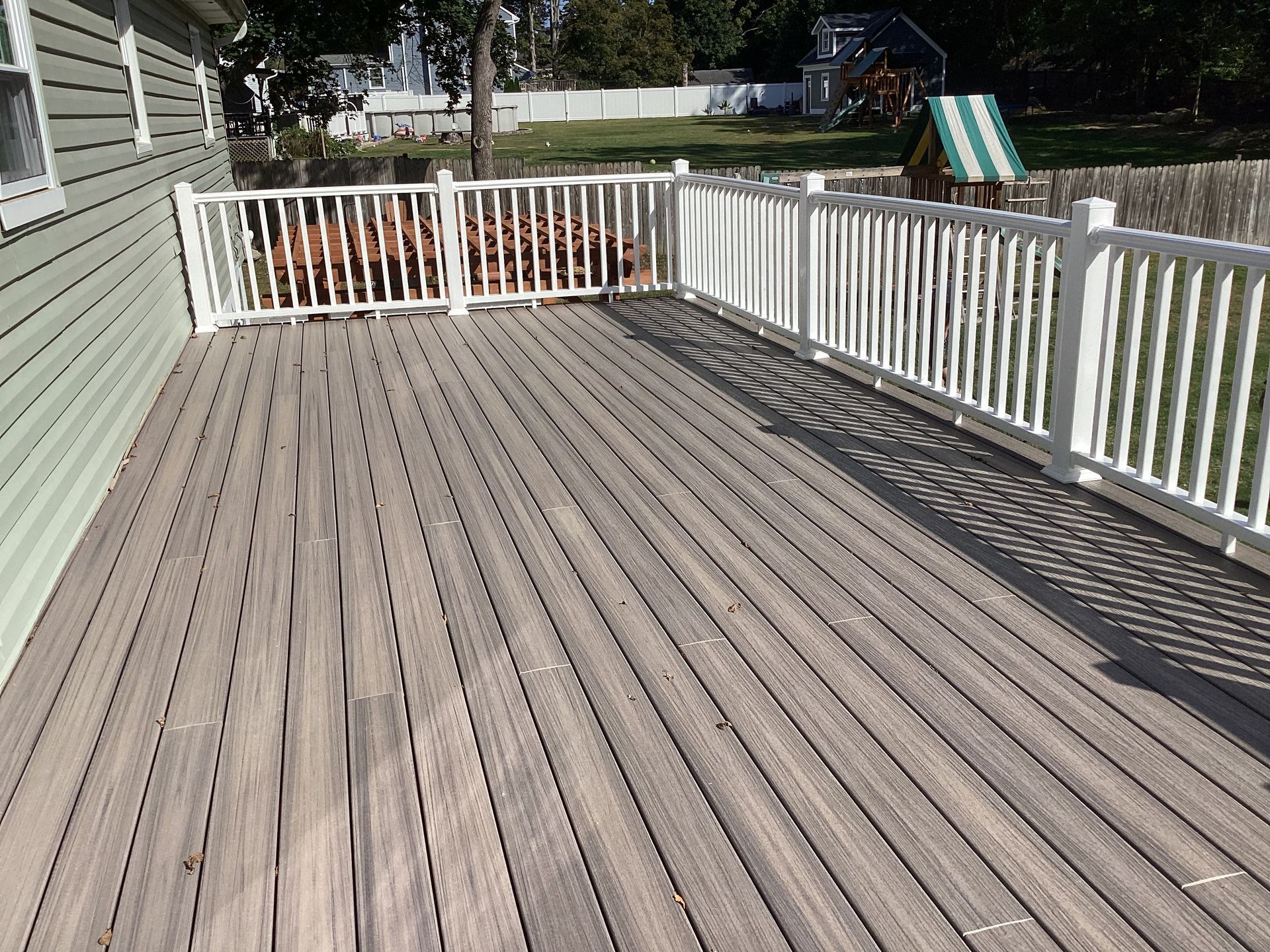 A wooden deck with white railings. Green siding and a yard with a playset are visible.