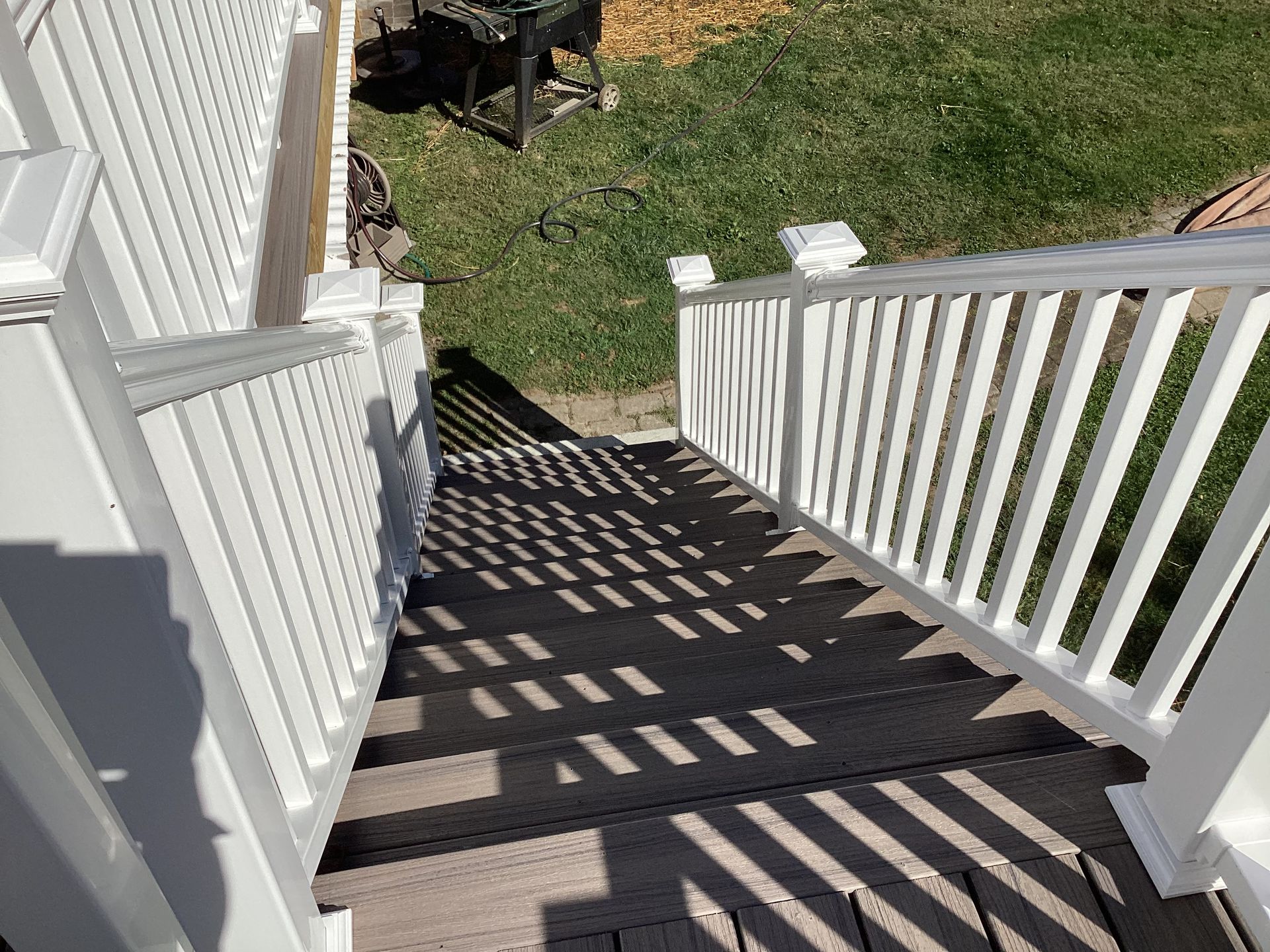 White railing staircase leading down to grassy yard. Shadows from railing bars on the steps.