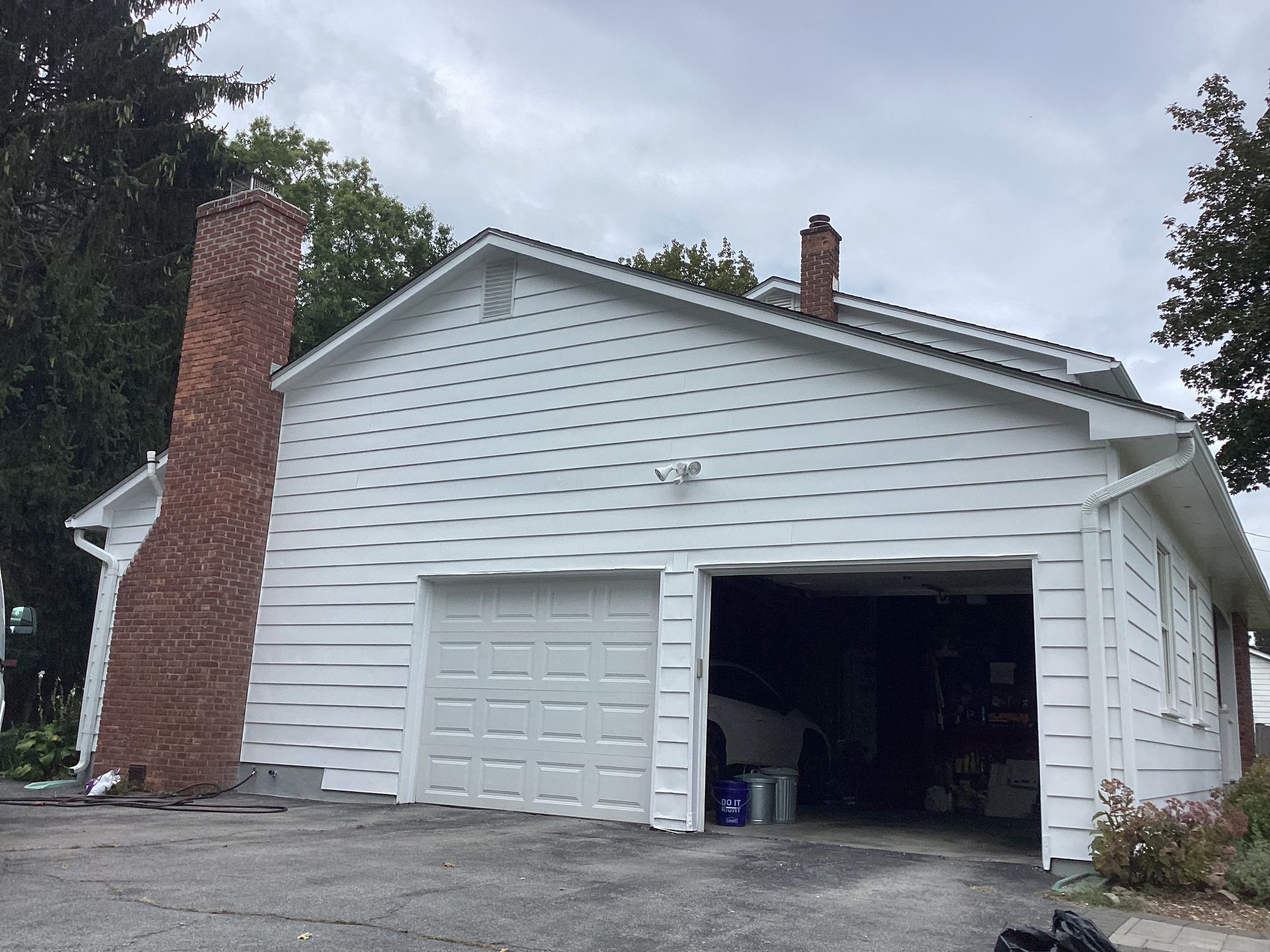 White garage with brick chimney, gray doors, and a cloudy sky.