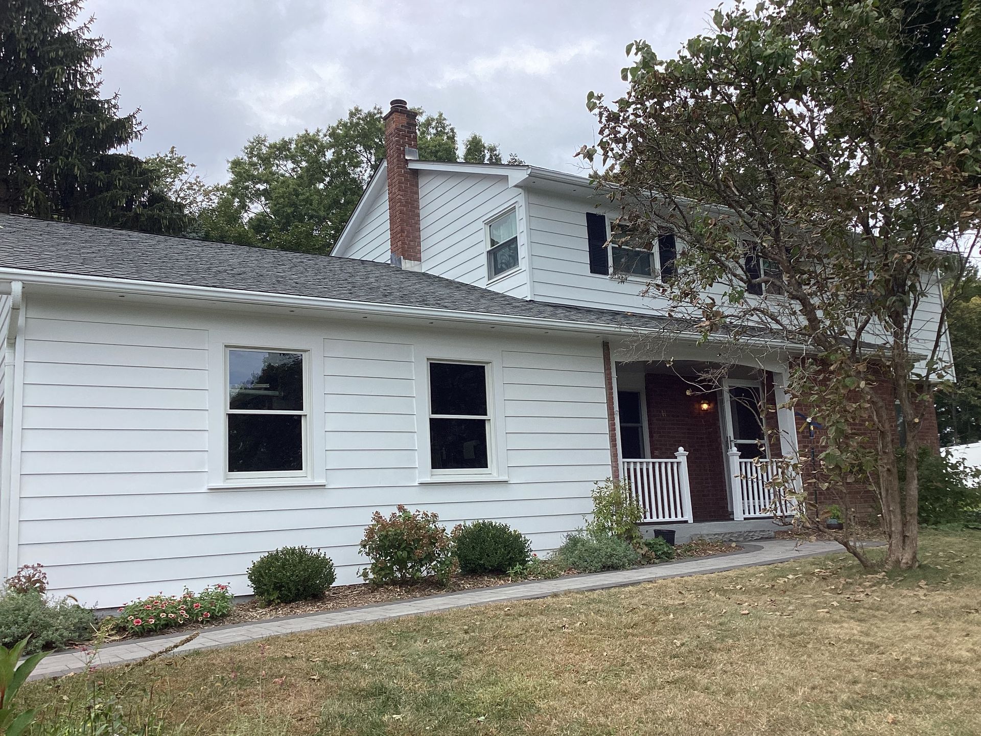 White two-story house with a small porch, windows, and chimney under an overcast sky.