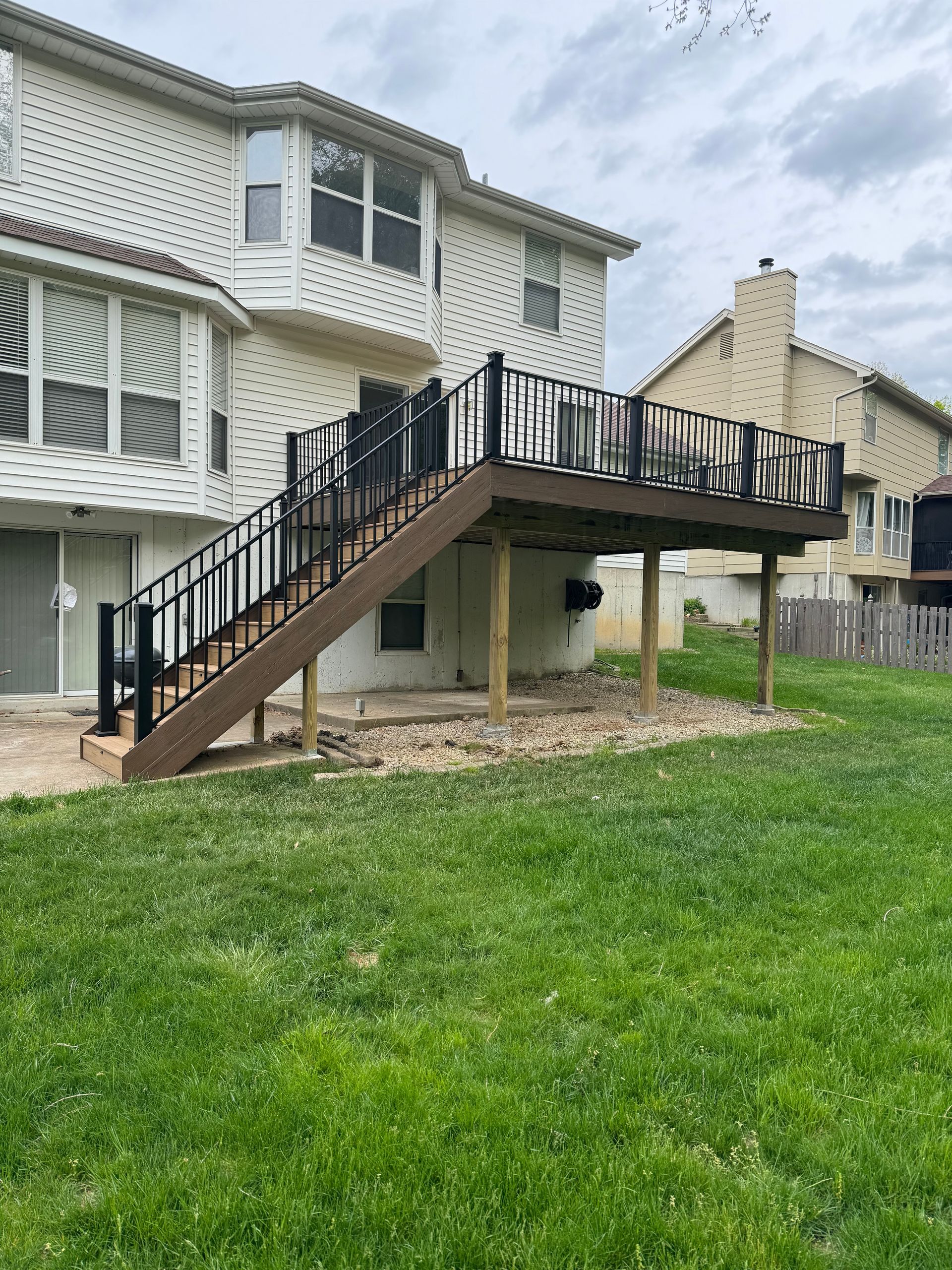 A deck with stairs leading up to it is in the backyard of a house.