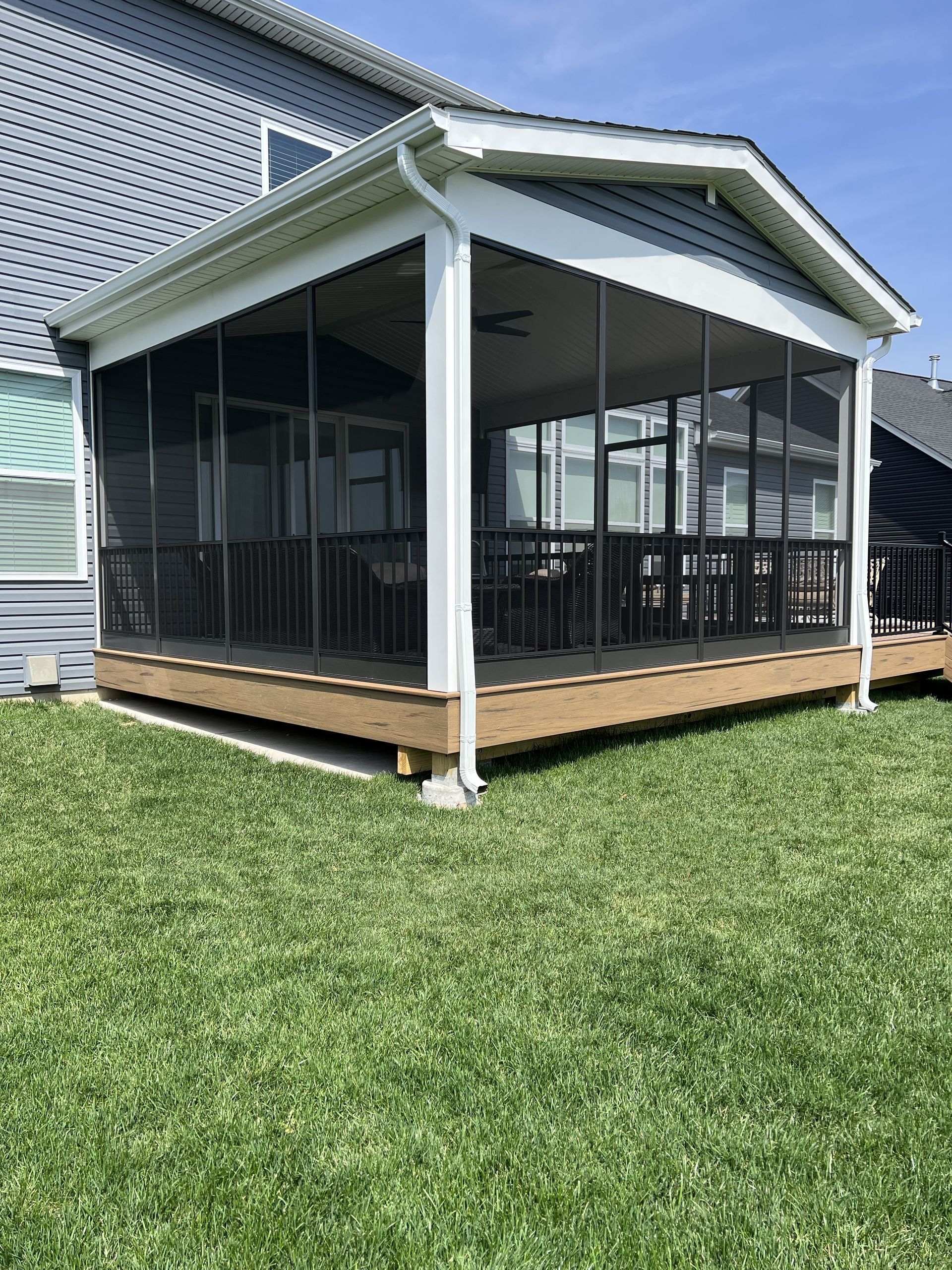 A screened-in porch with a wooden deck in the backyard of a house.