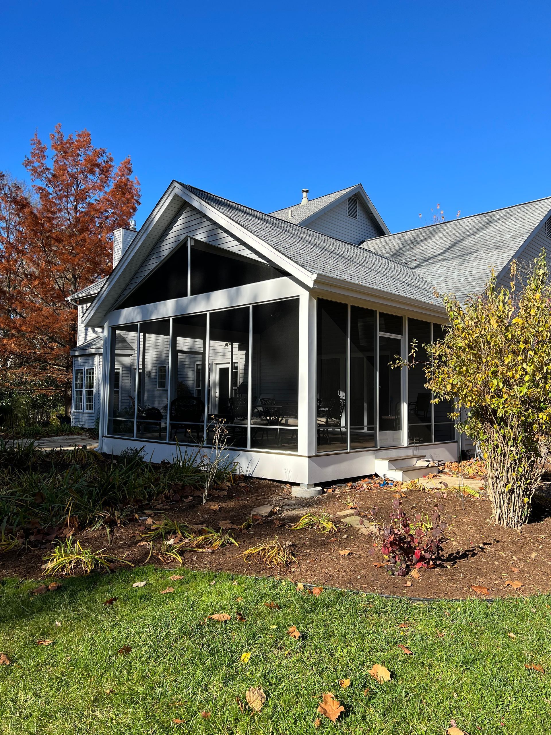 A house with a screened-in porch and a large lawn in front of it.