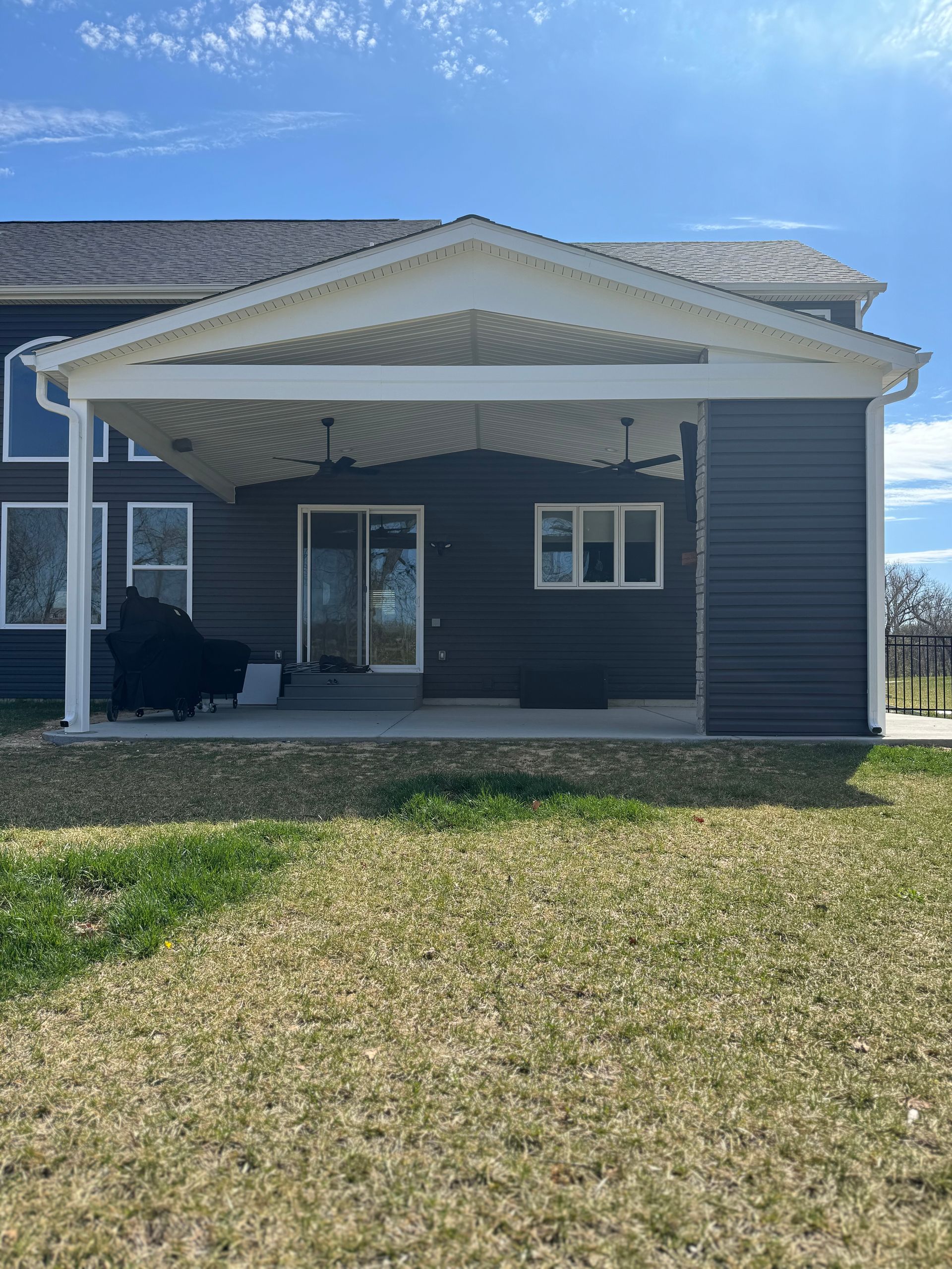 The back of a house with a covered porch and a large lawn in front of it.