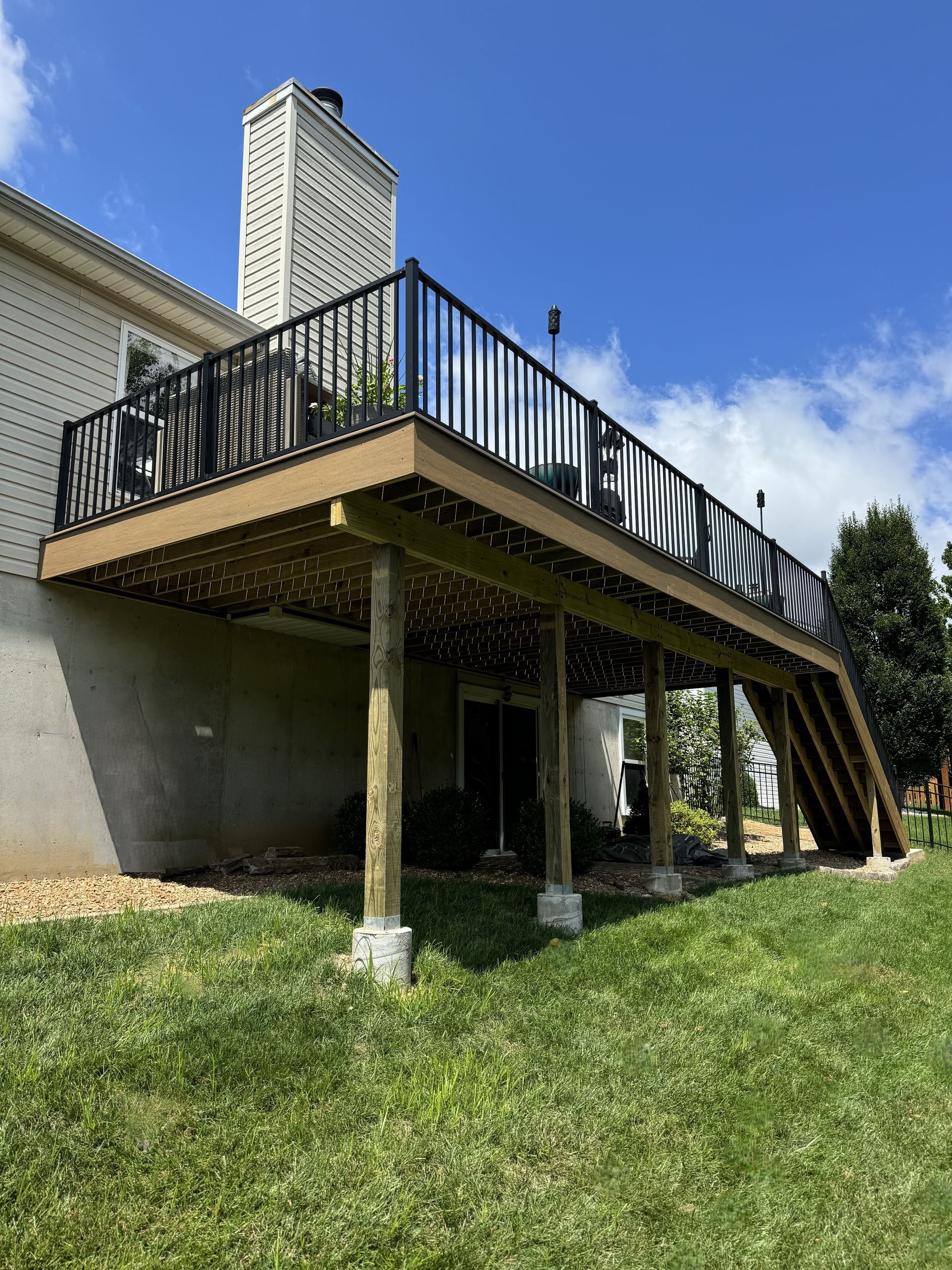 A large wooden deck with stairs leading up to it is in the backyard of a house.