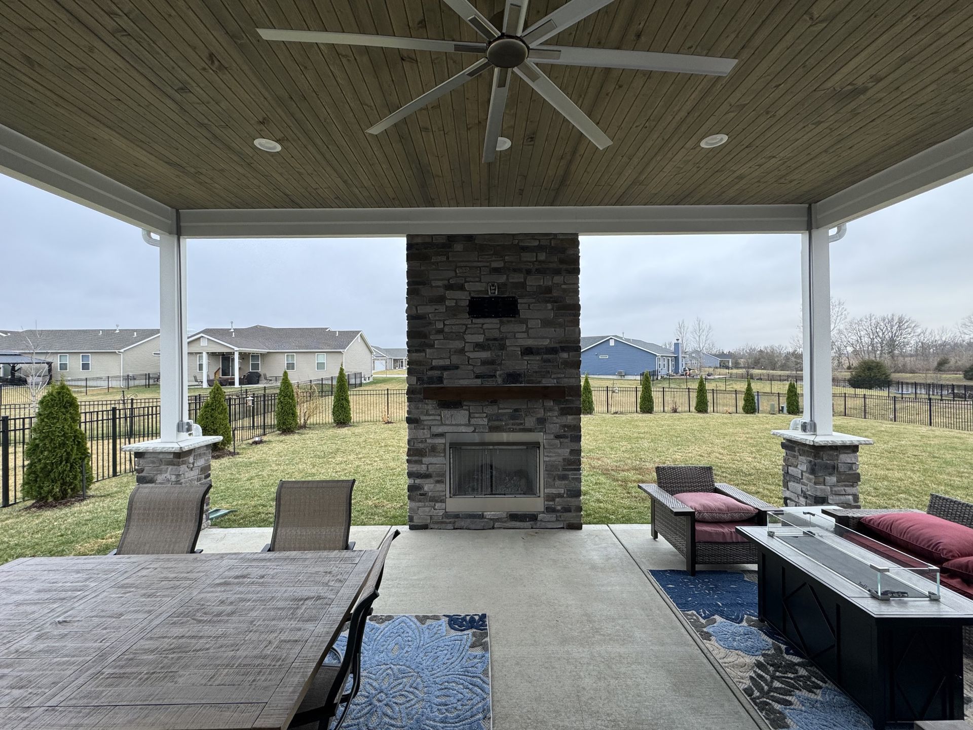 A patio with a fireplace , table , chairs and a ceiling fan.
