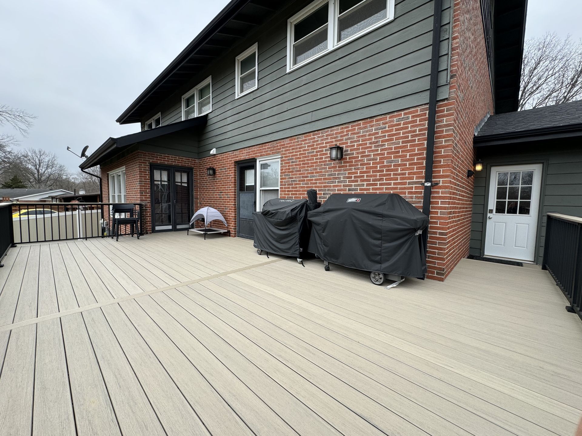 A large deck with a grill on it in front of a brick house.