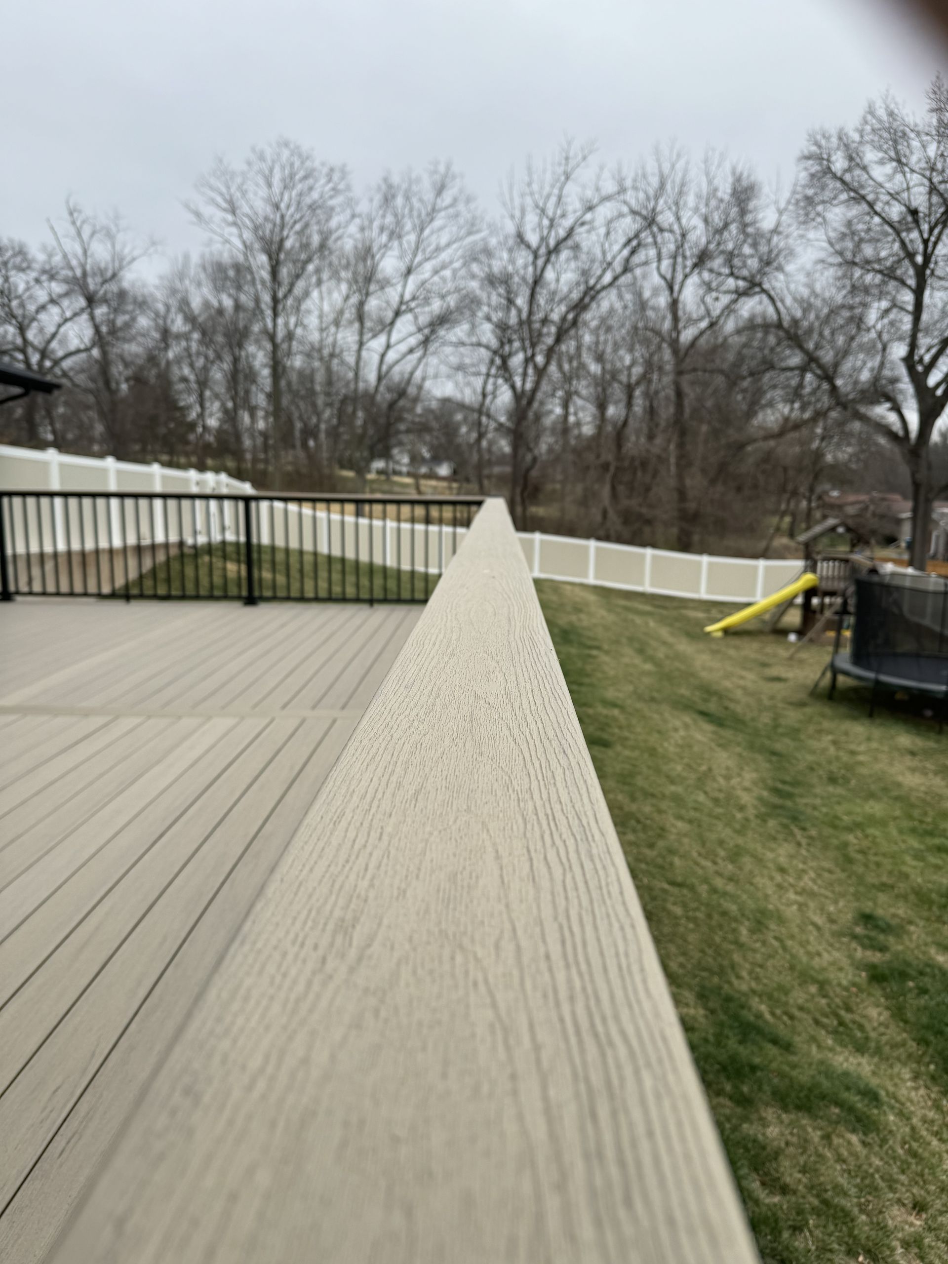 A wooden deck with a white fence and a playground in the background.