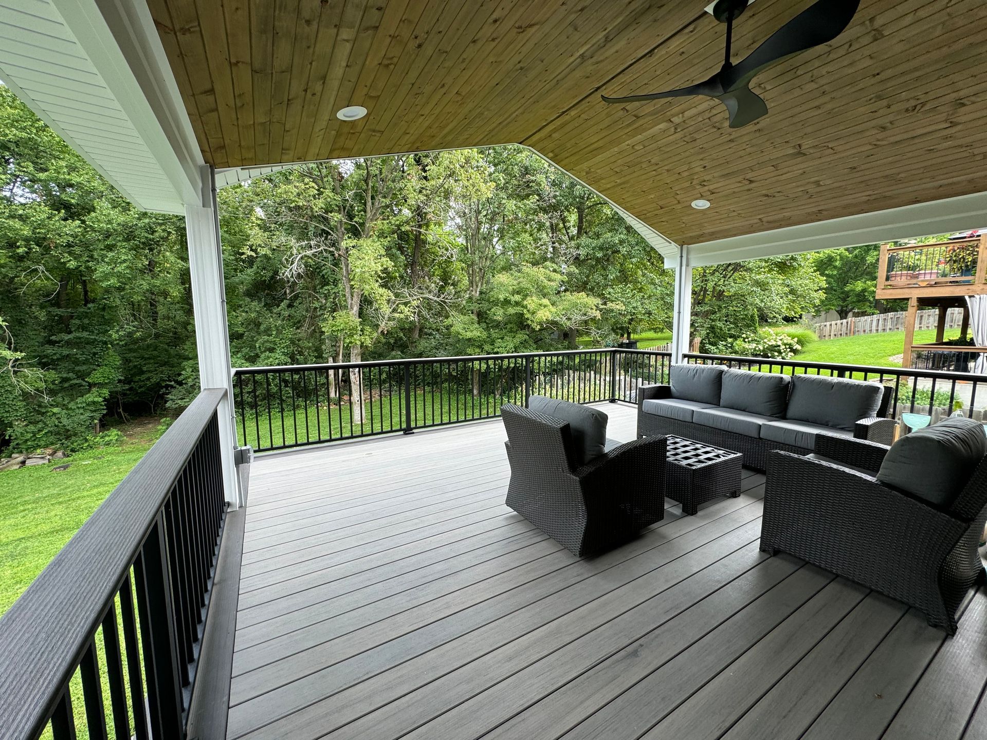 A large porch with a couch , chairs , and a ceiling fan.