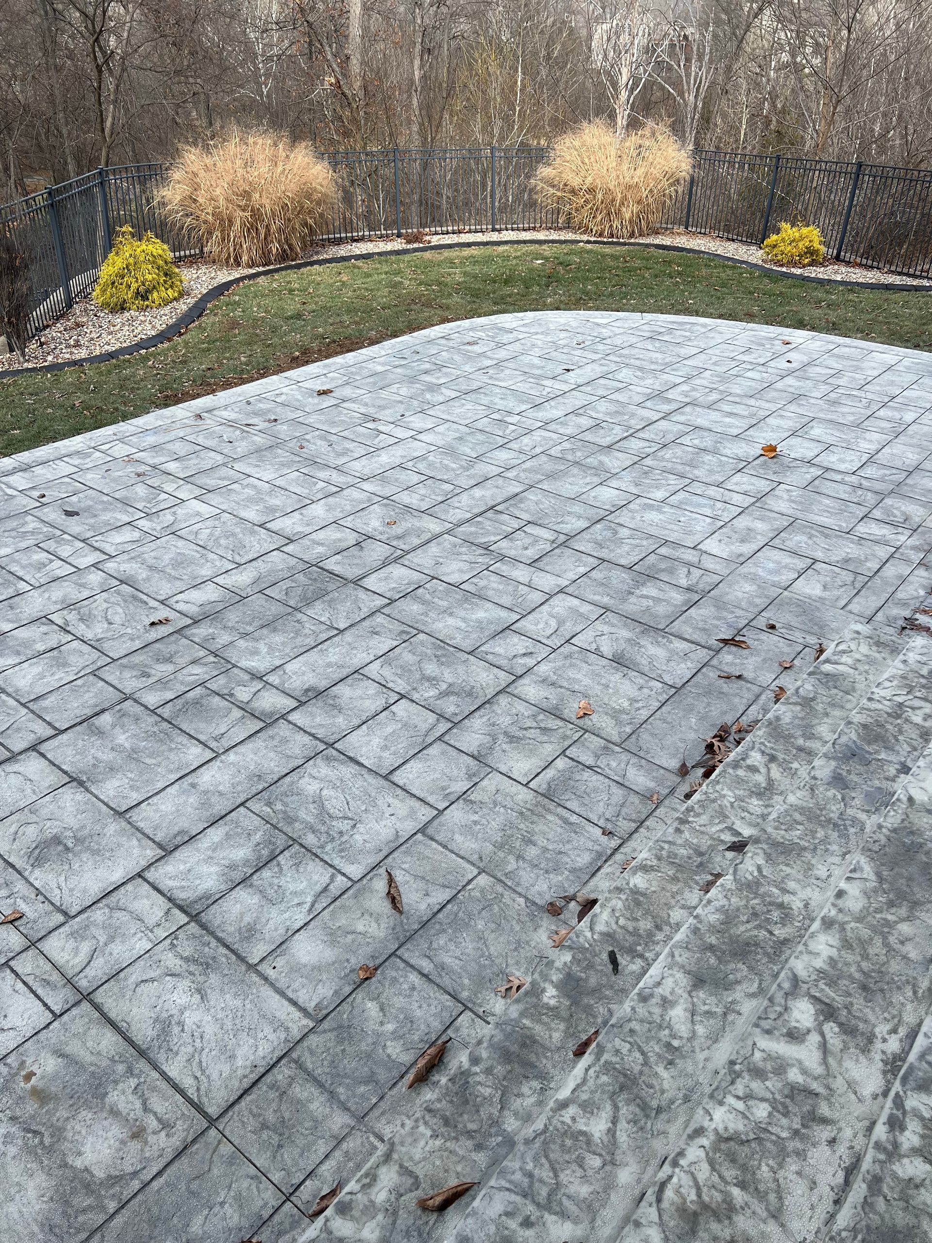 A concrete patio with a fence and grass in the background.