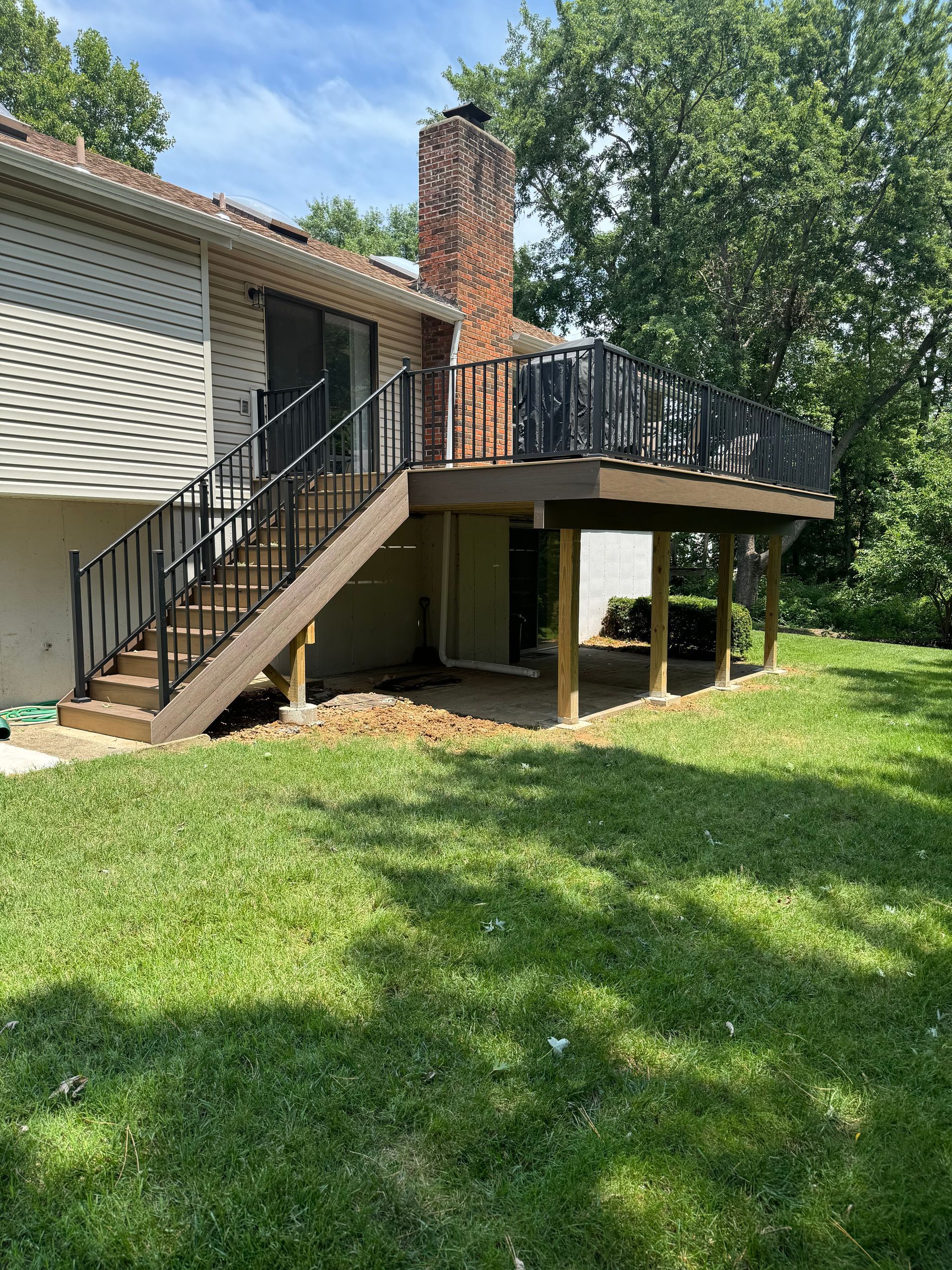 A large deck with stairs leading up to it is in the backyard of a house.