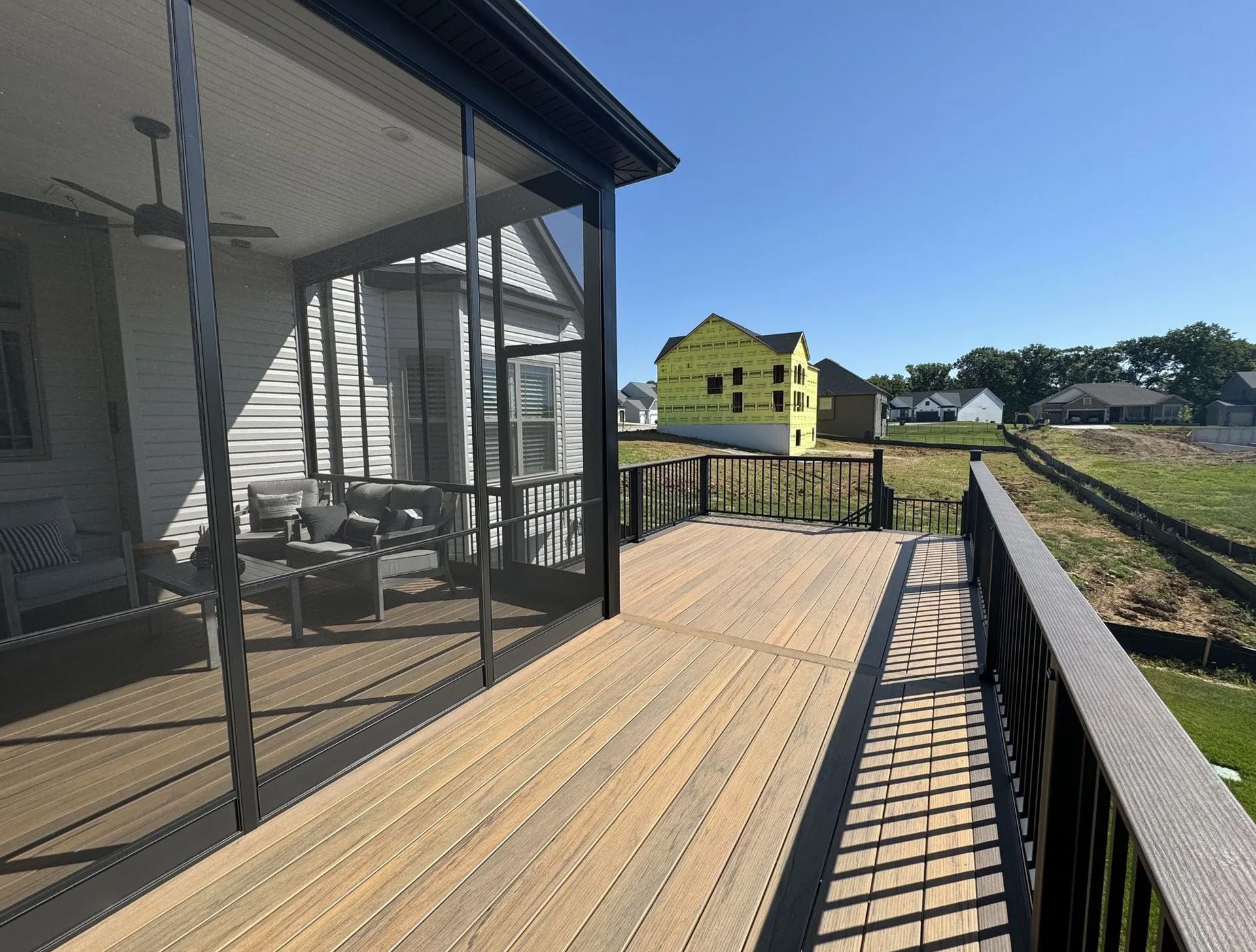 A screened in porch with a wooden deck and a yellow house in the background